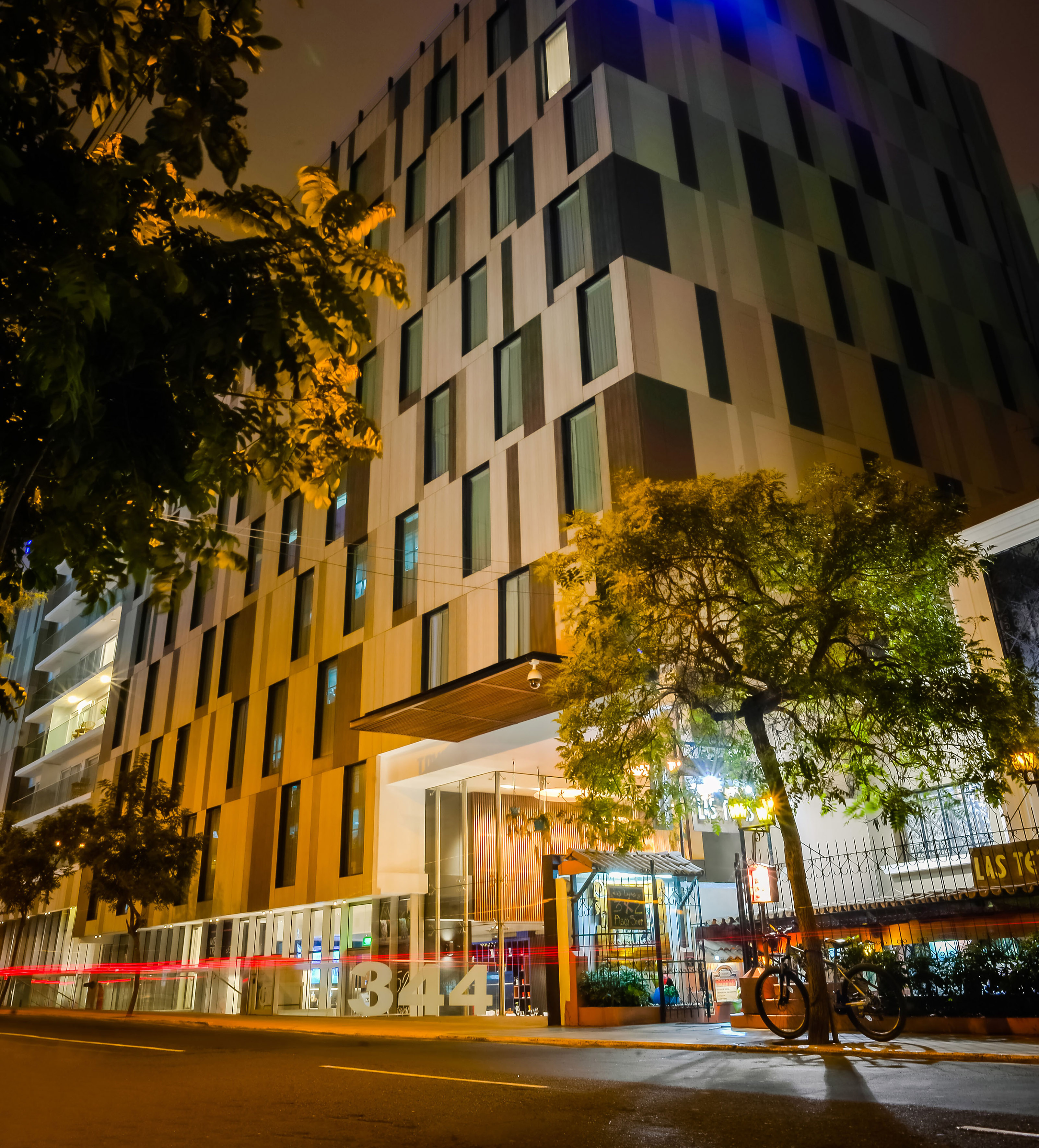 Illuminated modern hotel building at night, city street, trees, red light trails.