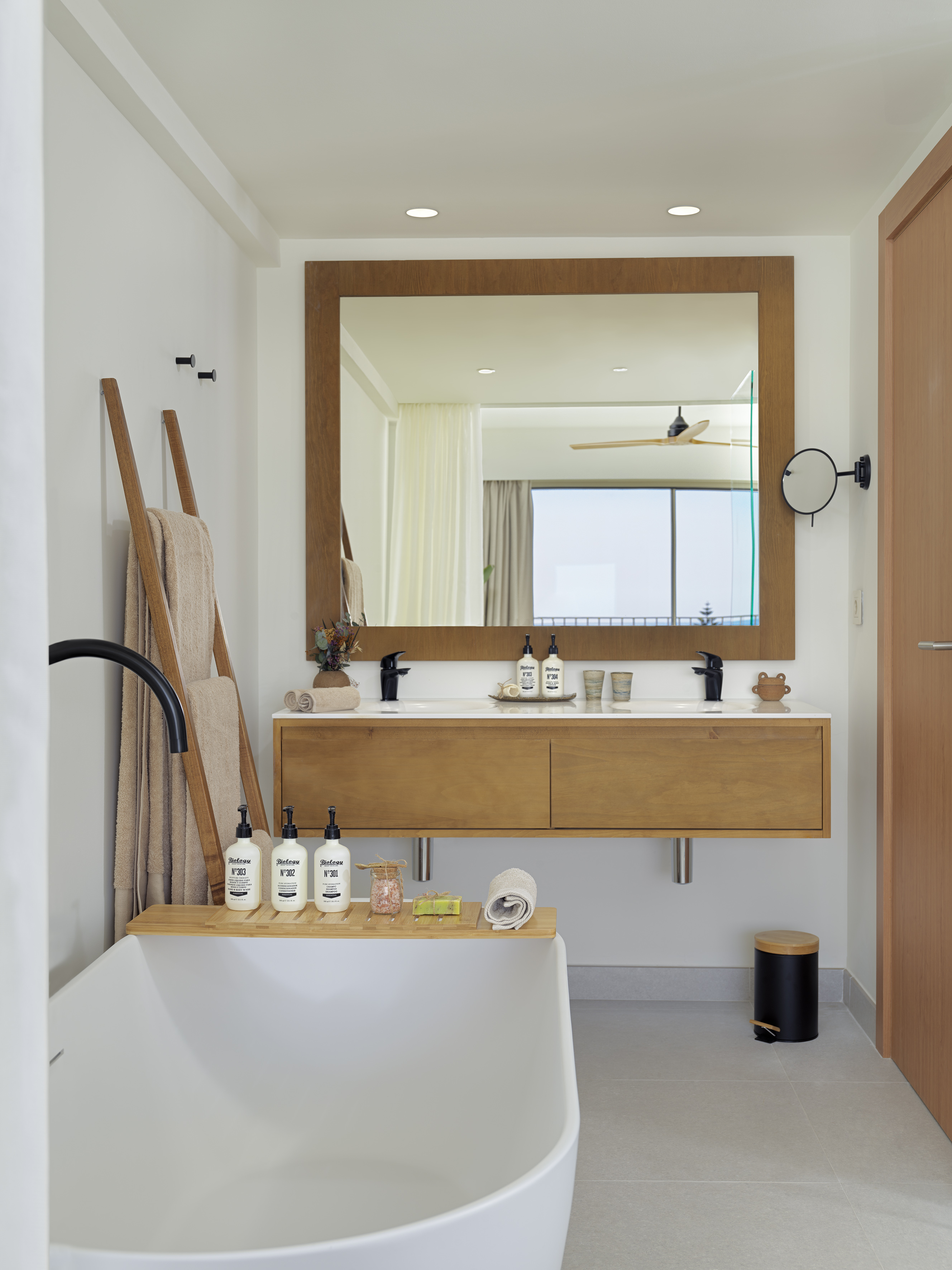 Modern bathroom with freestanding tub, wooden vanity, mirror, and spa amenities.