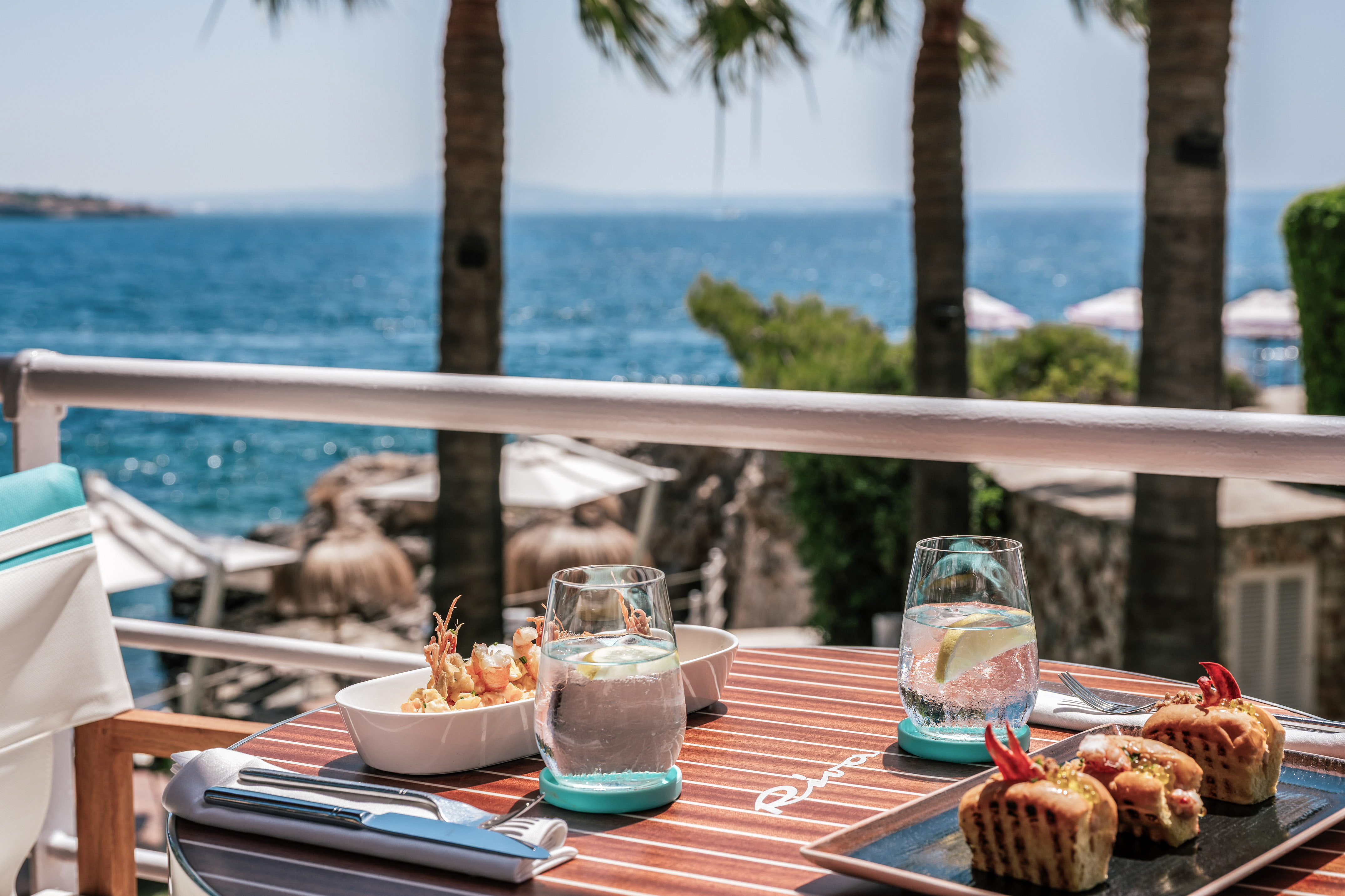 Gourmet seafood and drinks on an oceanfront terrace with palm trees.