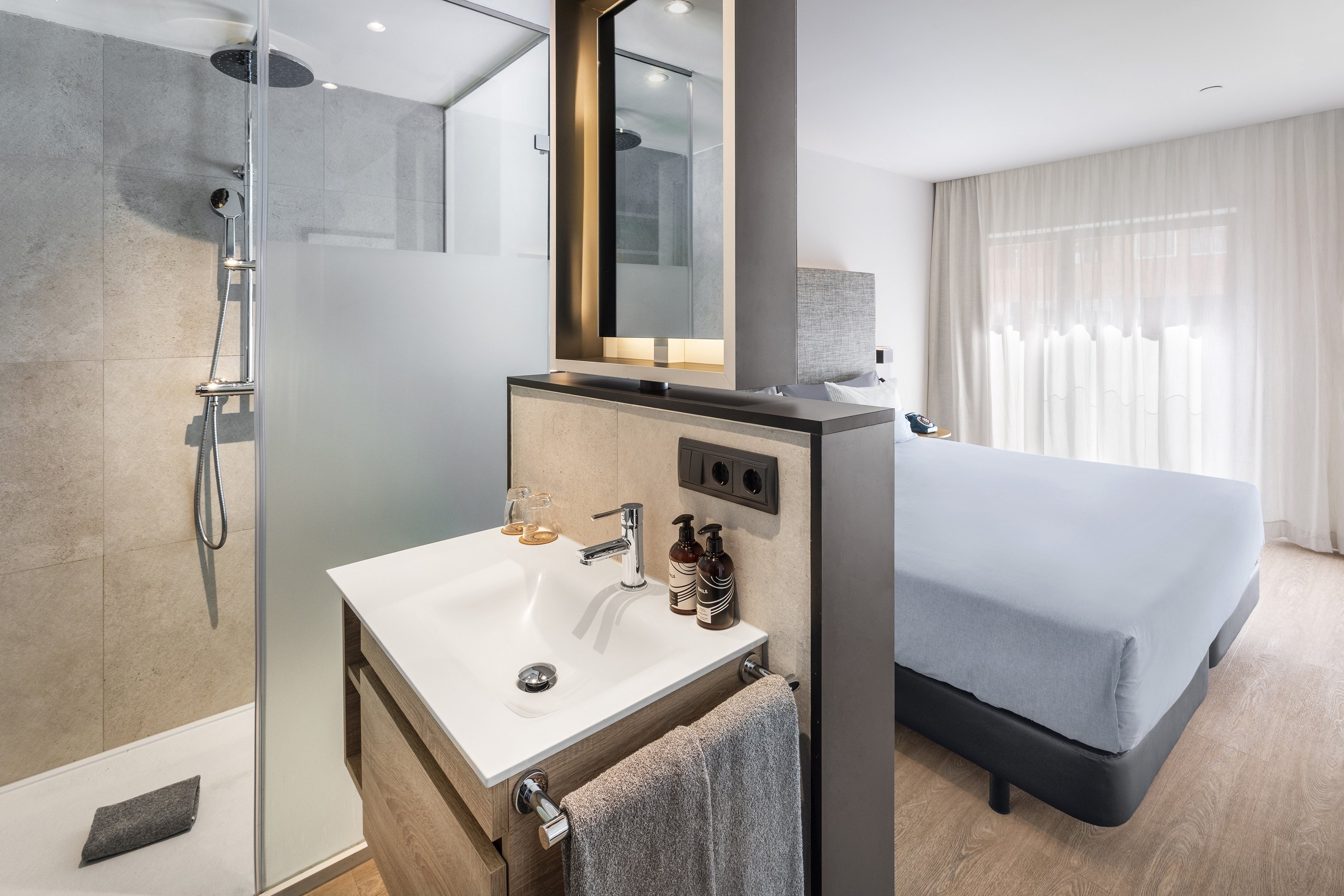 Modern hotel room with integrated bathroom, shower, vanity, and bedroom.
