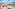 Sunny beach resort with pool, loungers, cabanas, palm trees, and blue ocean.