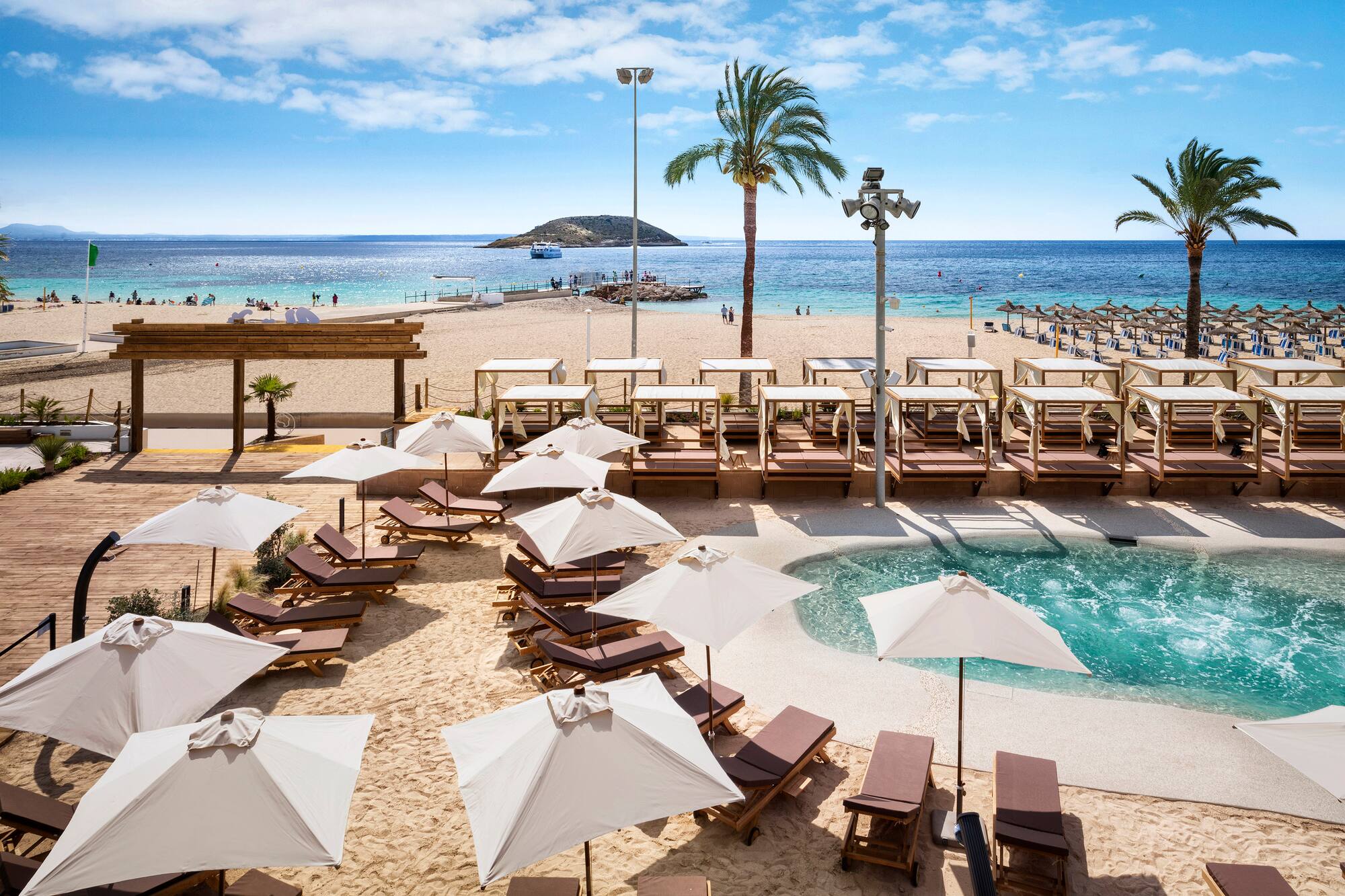 Sunny beach resort with pool, loungers, cabanas, palm trees, and blue ocean.