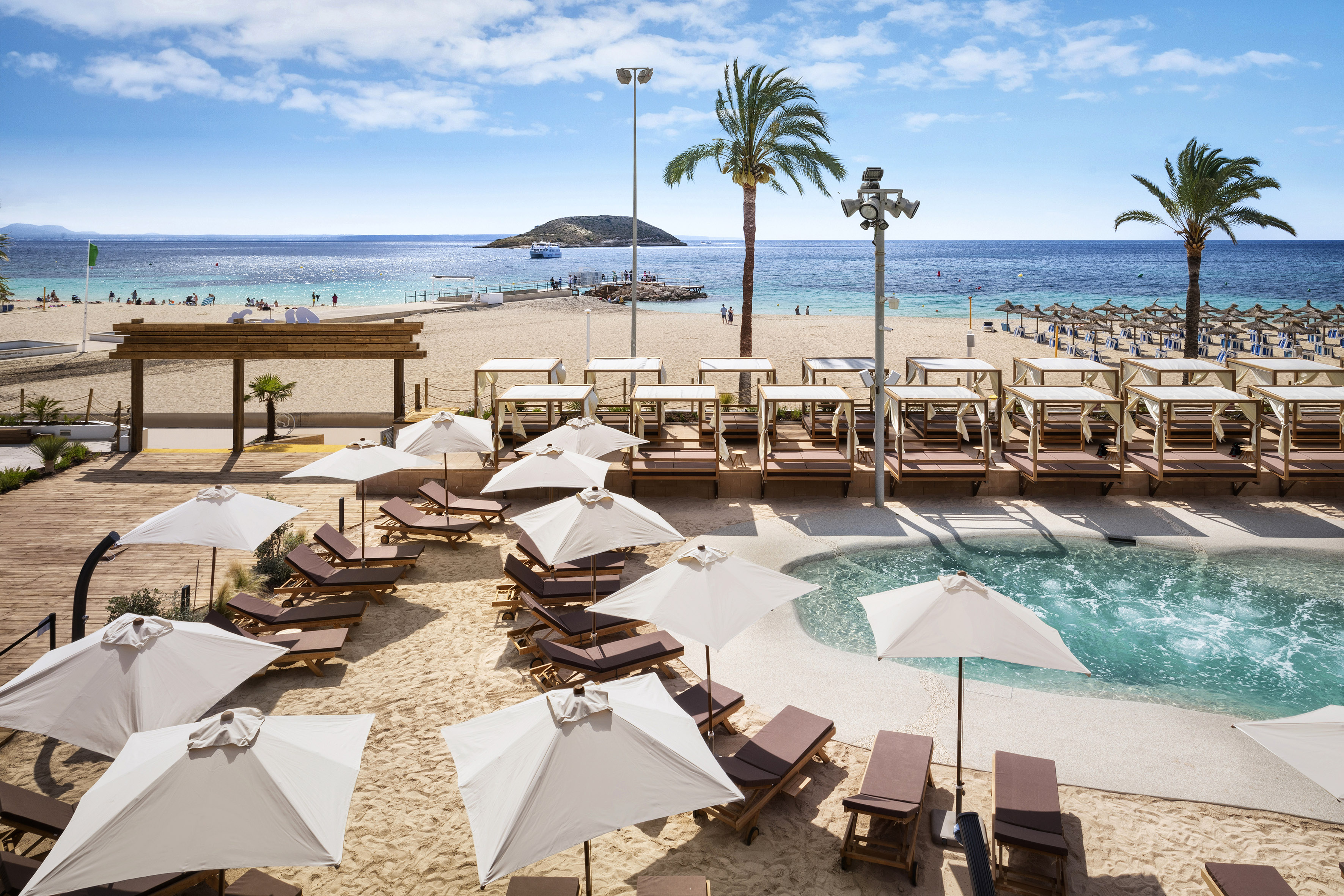 Sunny beach resort with pool, loungers, cabanas, palm trees, and blue ocean.
