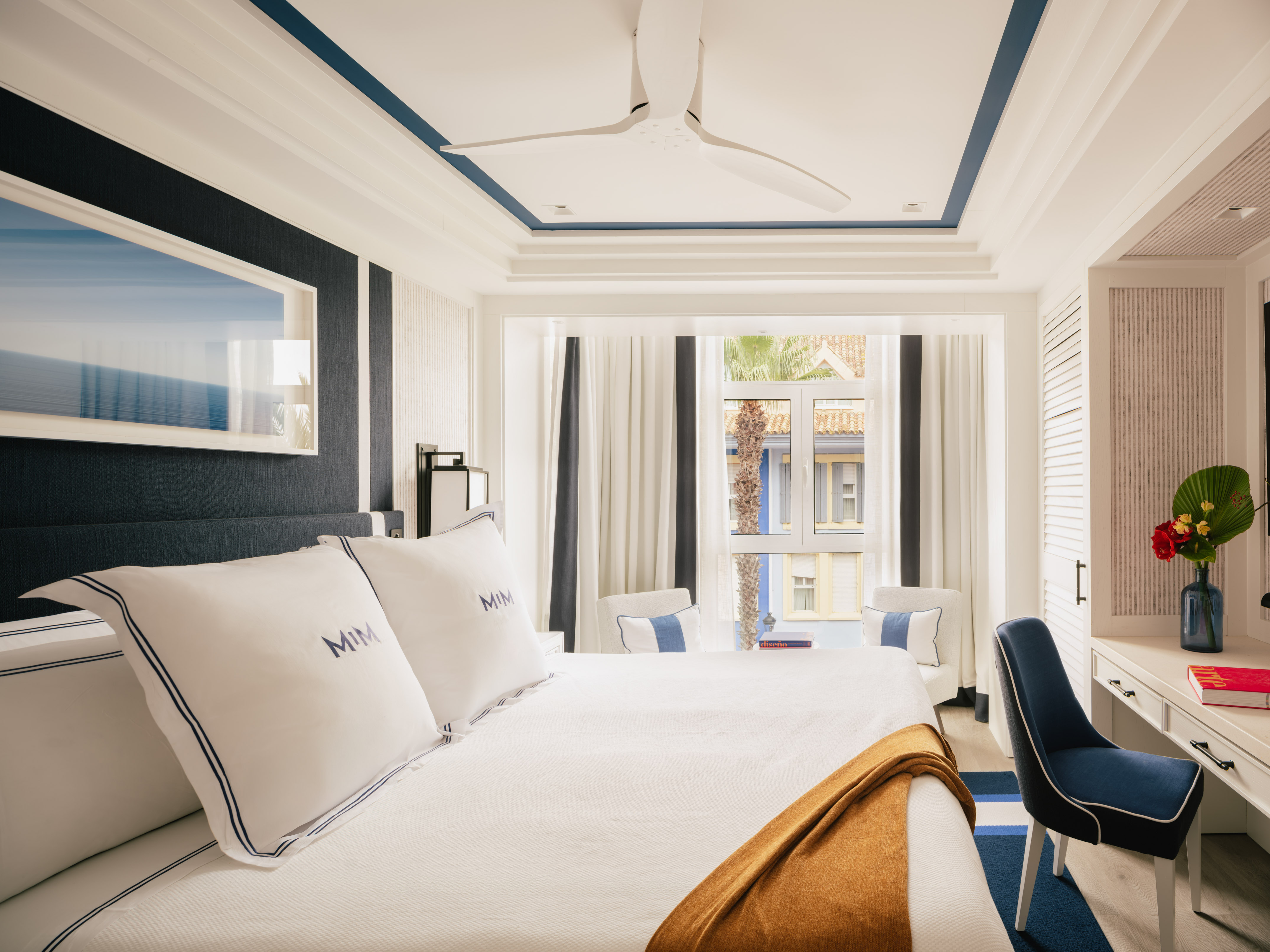 Luxury hotel bedroom with white king bed, navy blue accents, and large window.