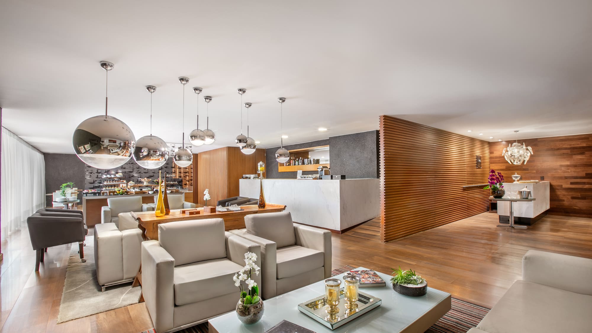 Modern hotel lobby with stylish seating, wood panels, marble counter, and buffet.