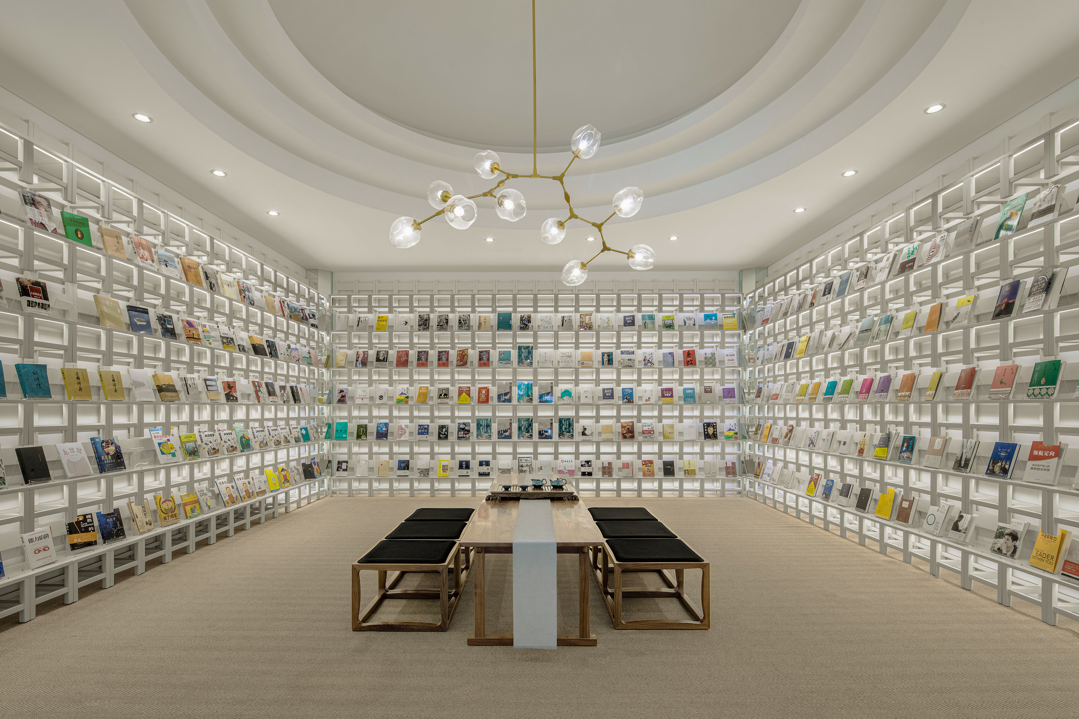 Minimalist library with white bookshelves, wooden reading table, and modern chandelier.