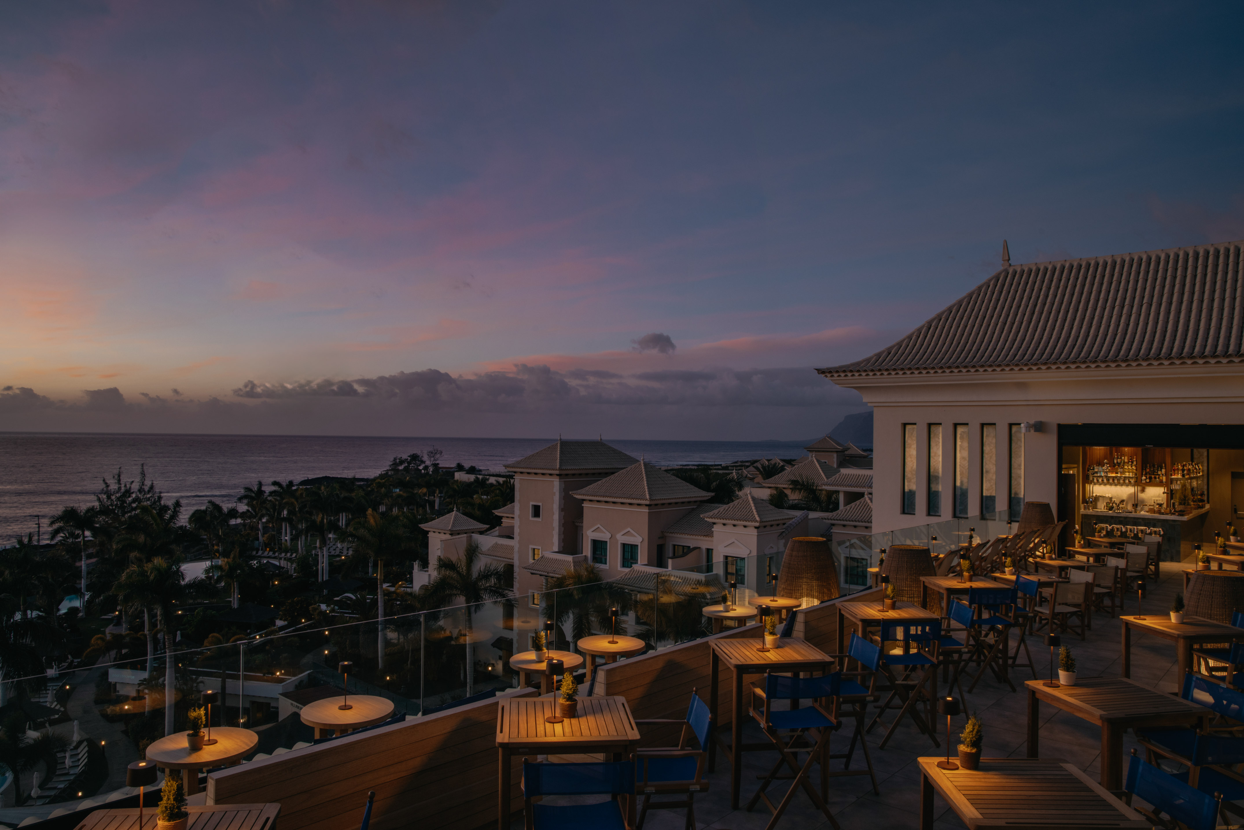 Twilight ocean view from a resort rooftop bar, outdoor dining setup.
