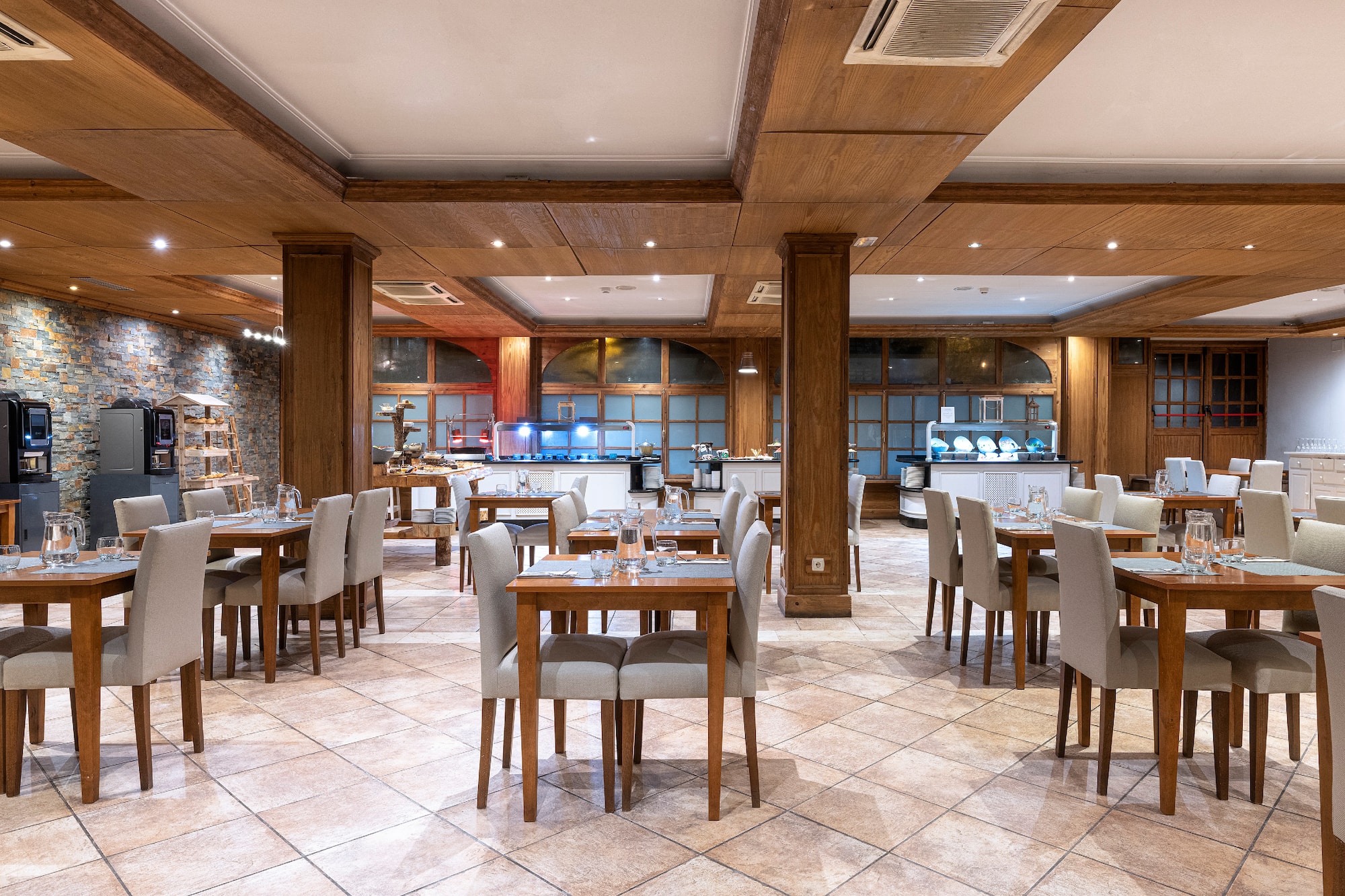 Restaurante de hotel con mesas, sillas, área de buffet y detalles de madera.
