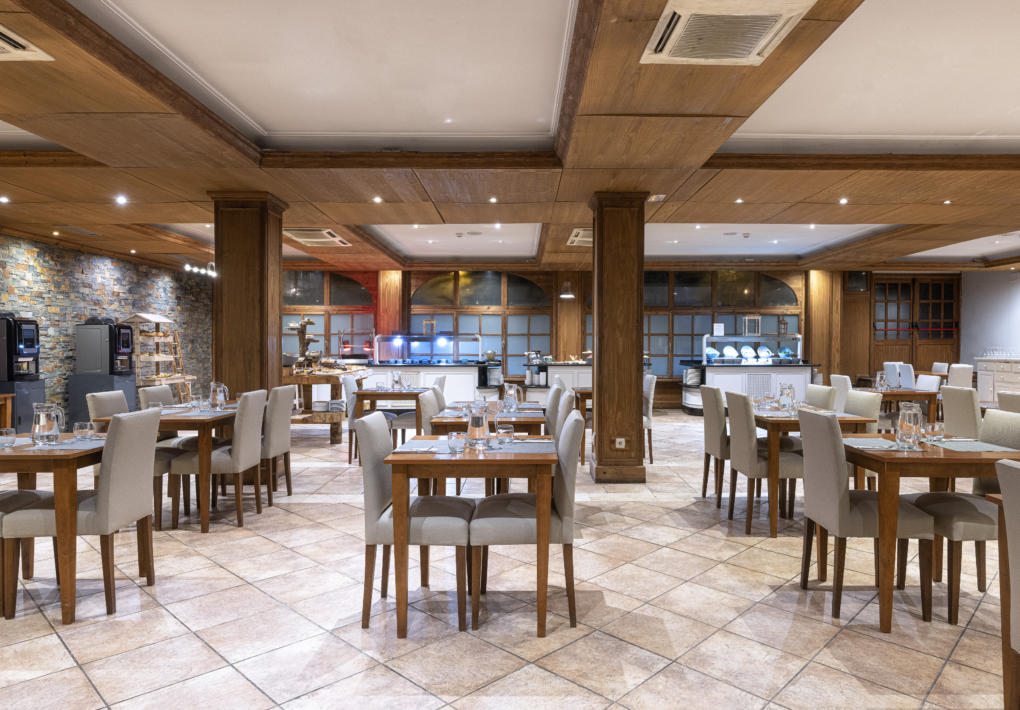 Restaurante de hotel con mesas, sillas, área de buffet y detalles de madera.