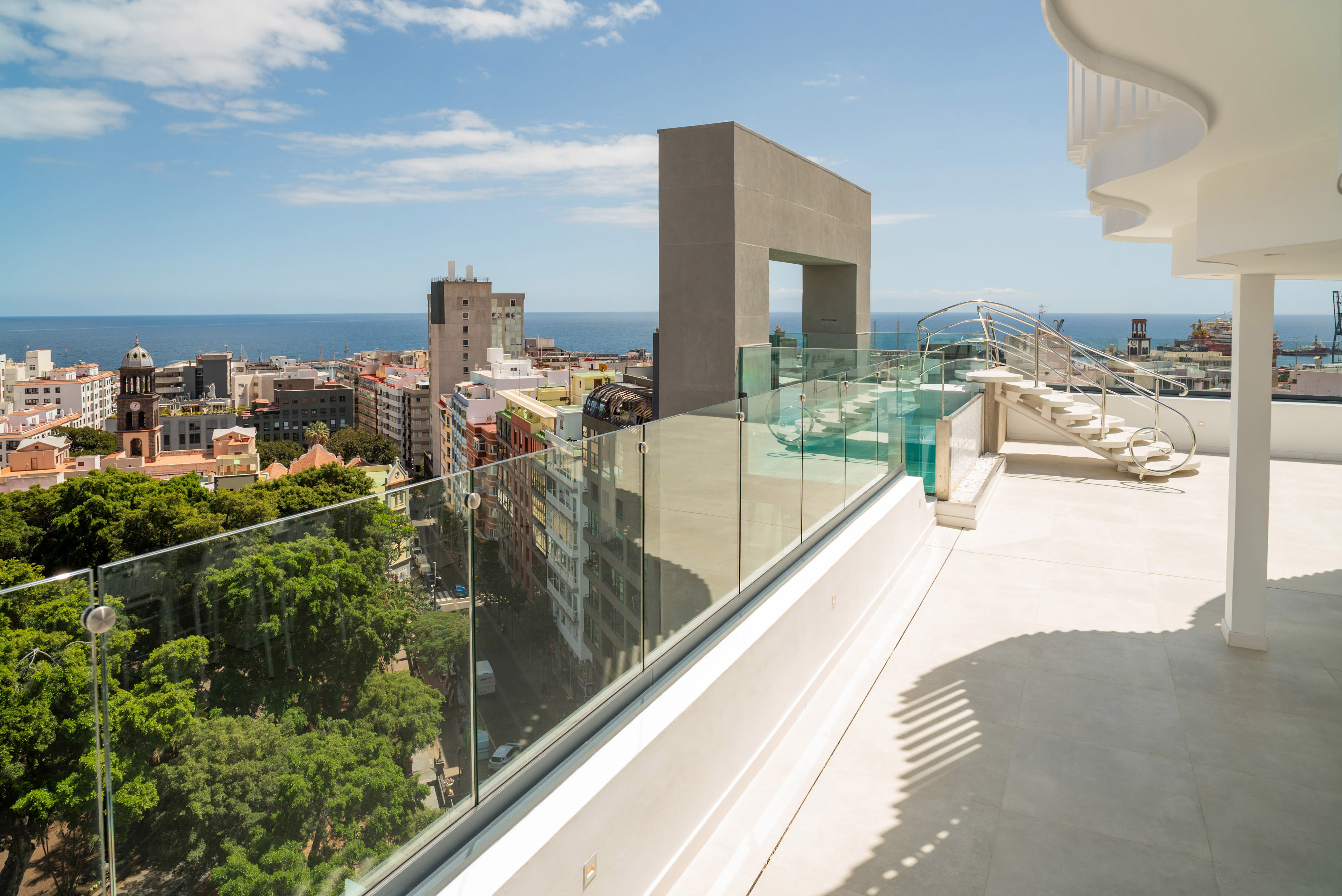 Modern rooftop terrace with city and ocean views, spiral stairs, and glass railing.
