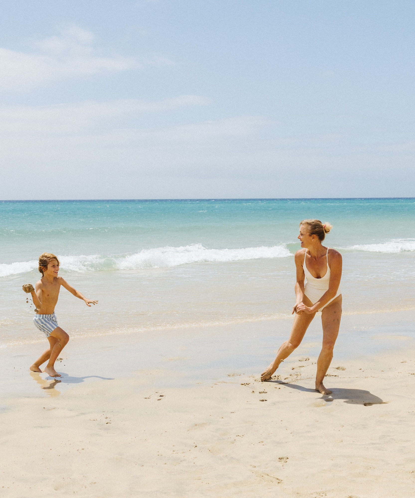 Woman and child playing on a sunny beach with ocean and kites.