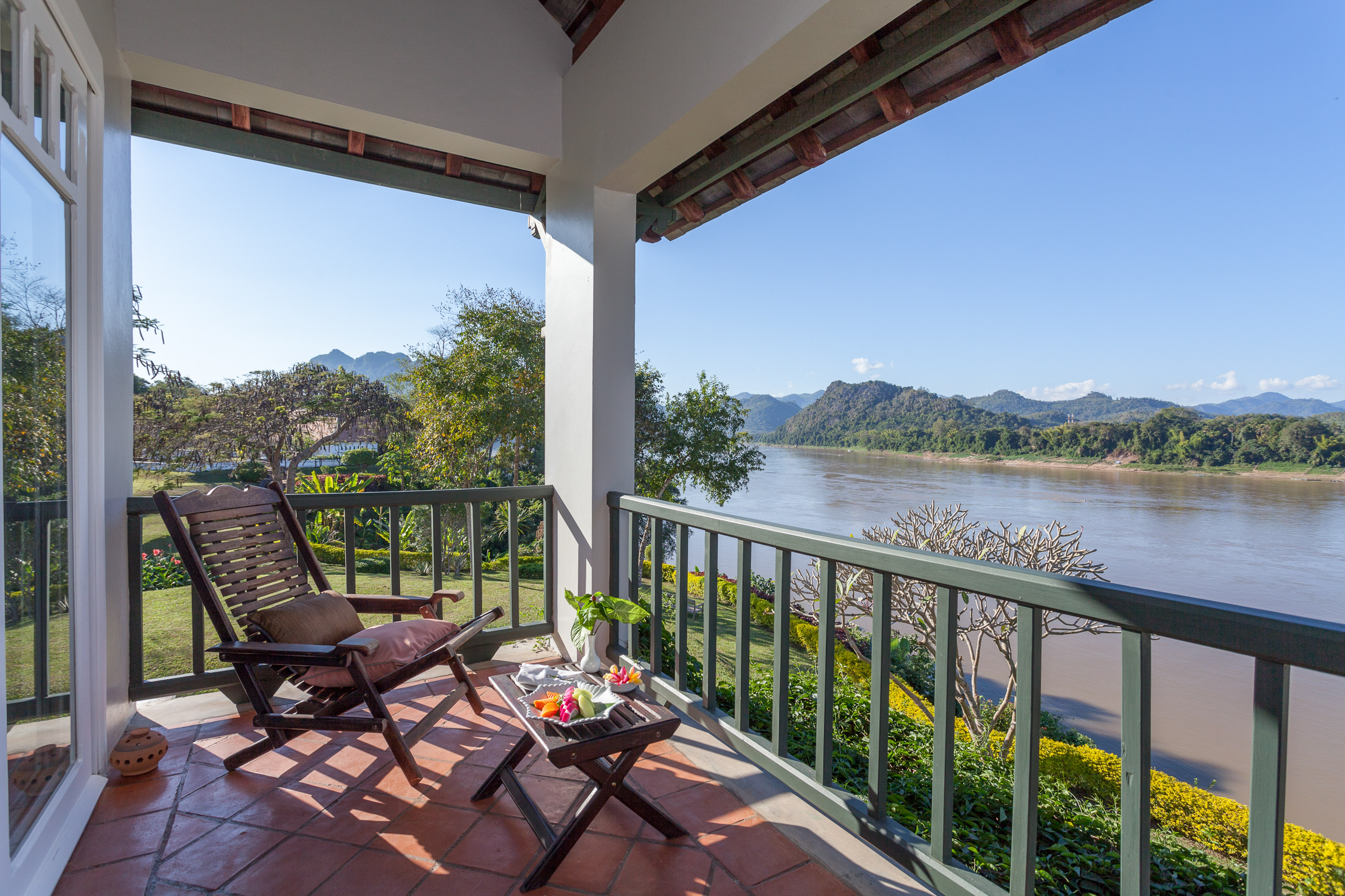 Scenic balcony with river and mountain views, wooden chair, snack table.