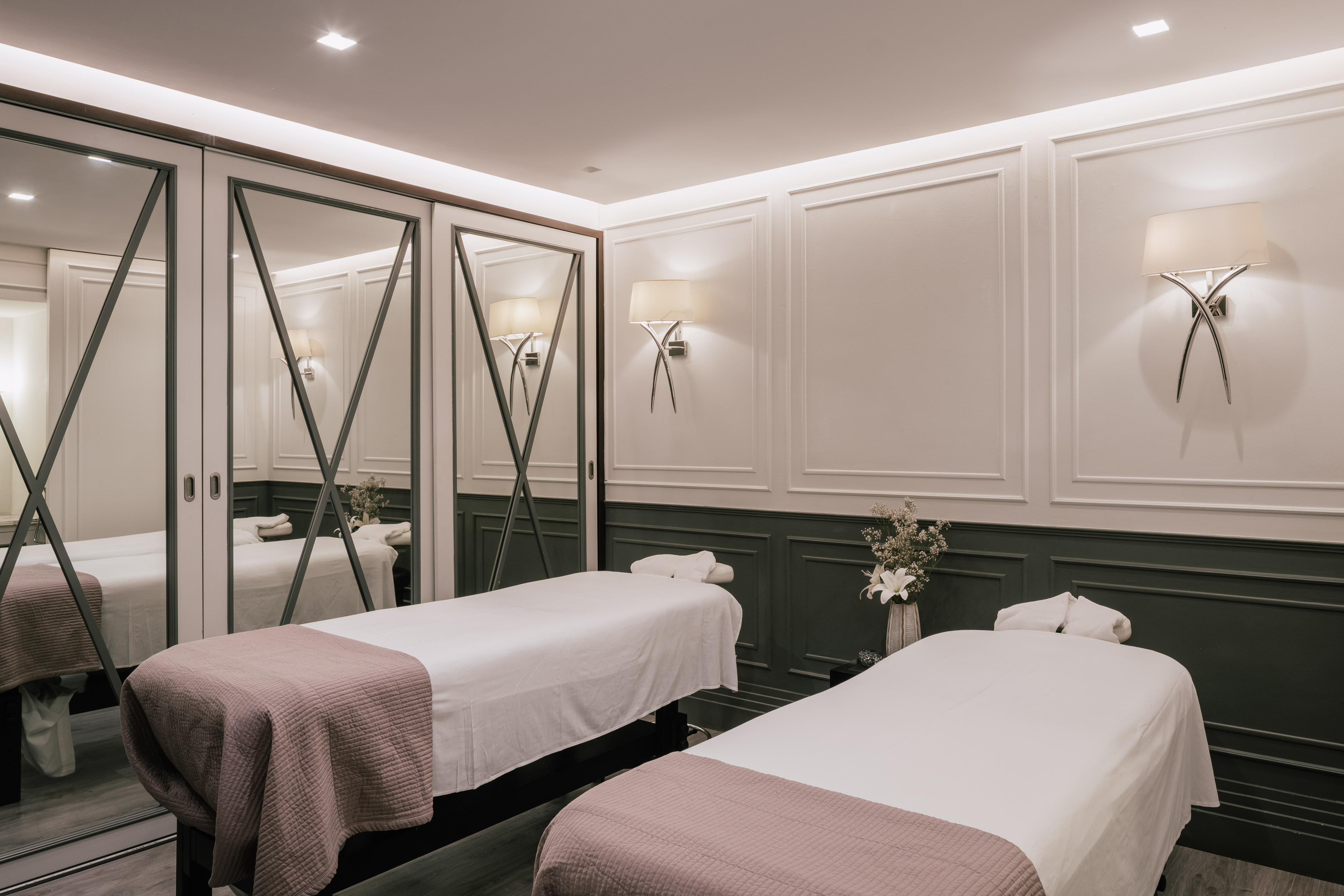 Elegant spa massage room with two therapy beds, mirrored walls, and sconces.