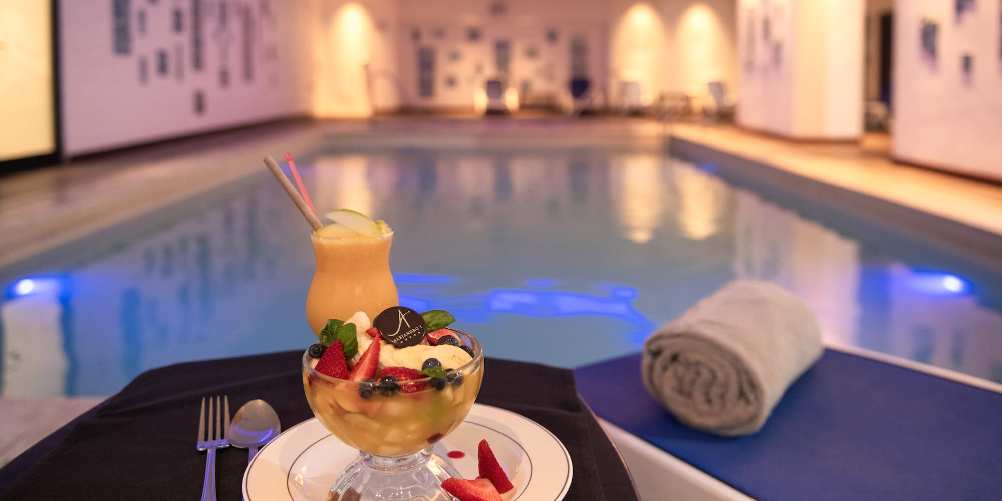 a bowl of fruit and a drink on a plate next to a pool