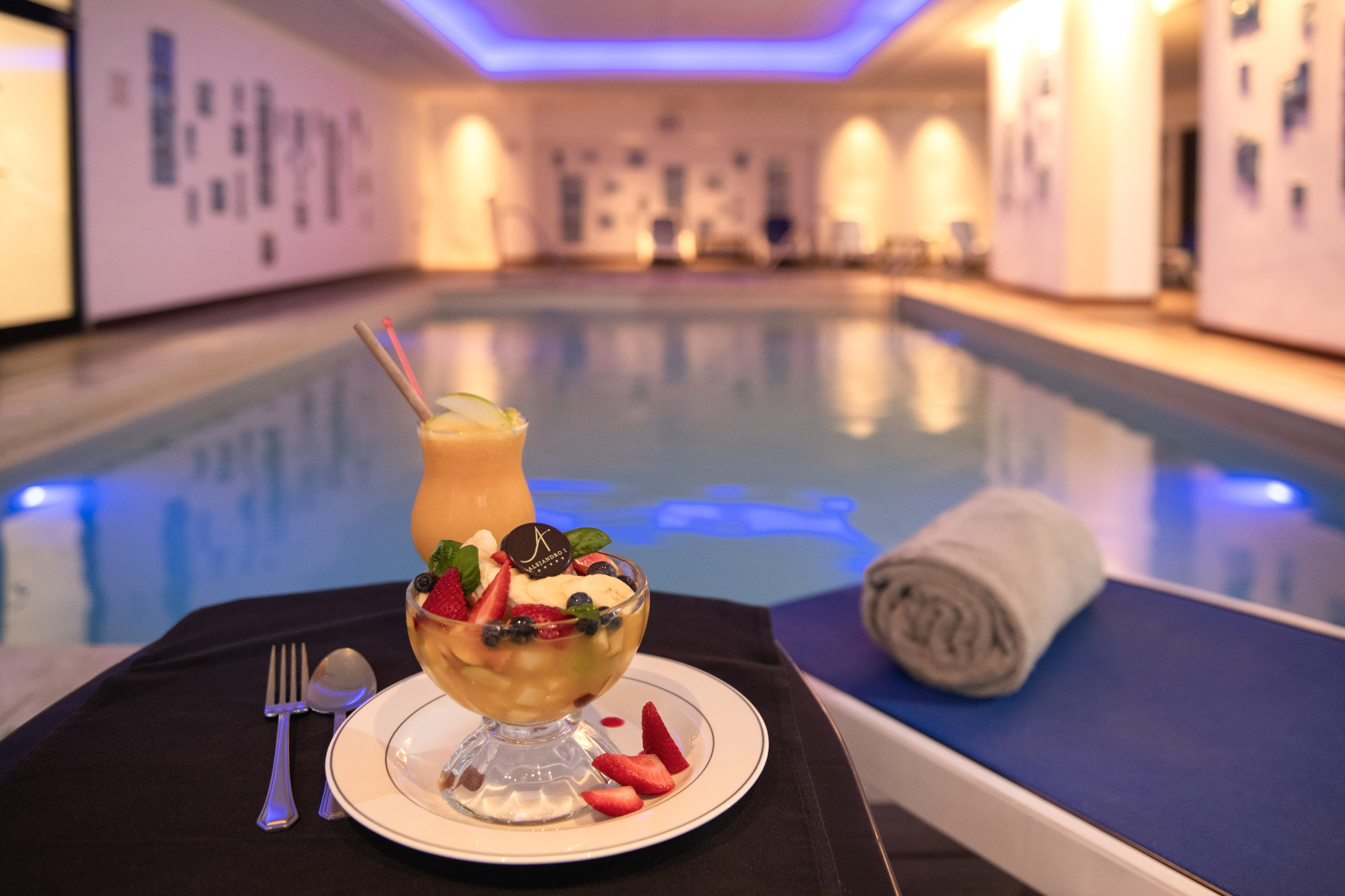 Refreshing fruit salad and smoothie by a hotel's blue-lit indoor pool.