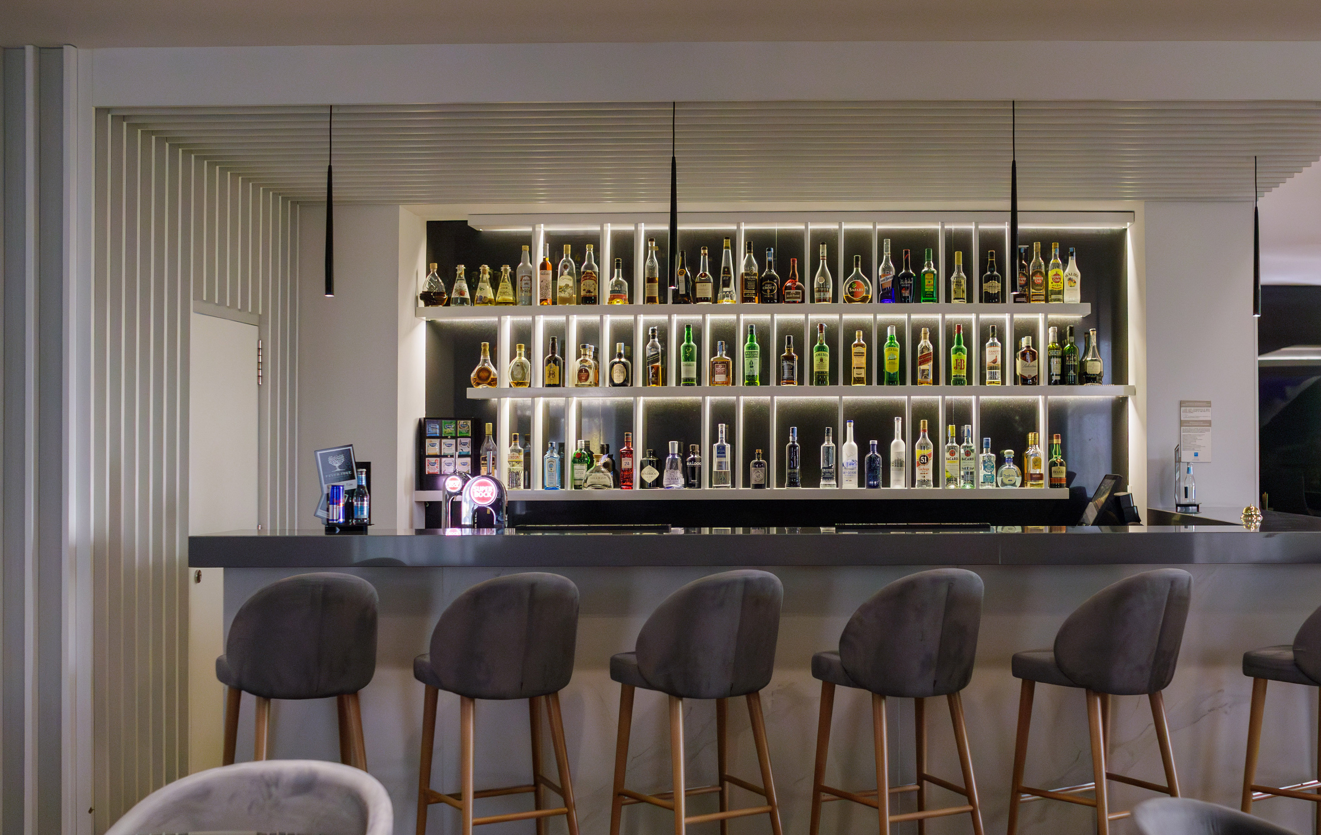 Stylish hotel bar with illuminated liquor bottles and modern stools.