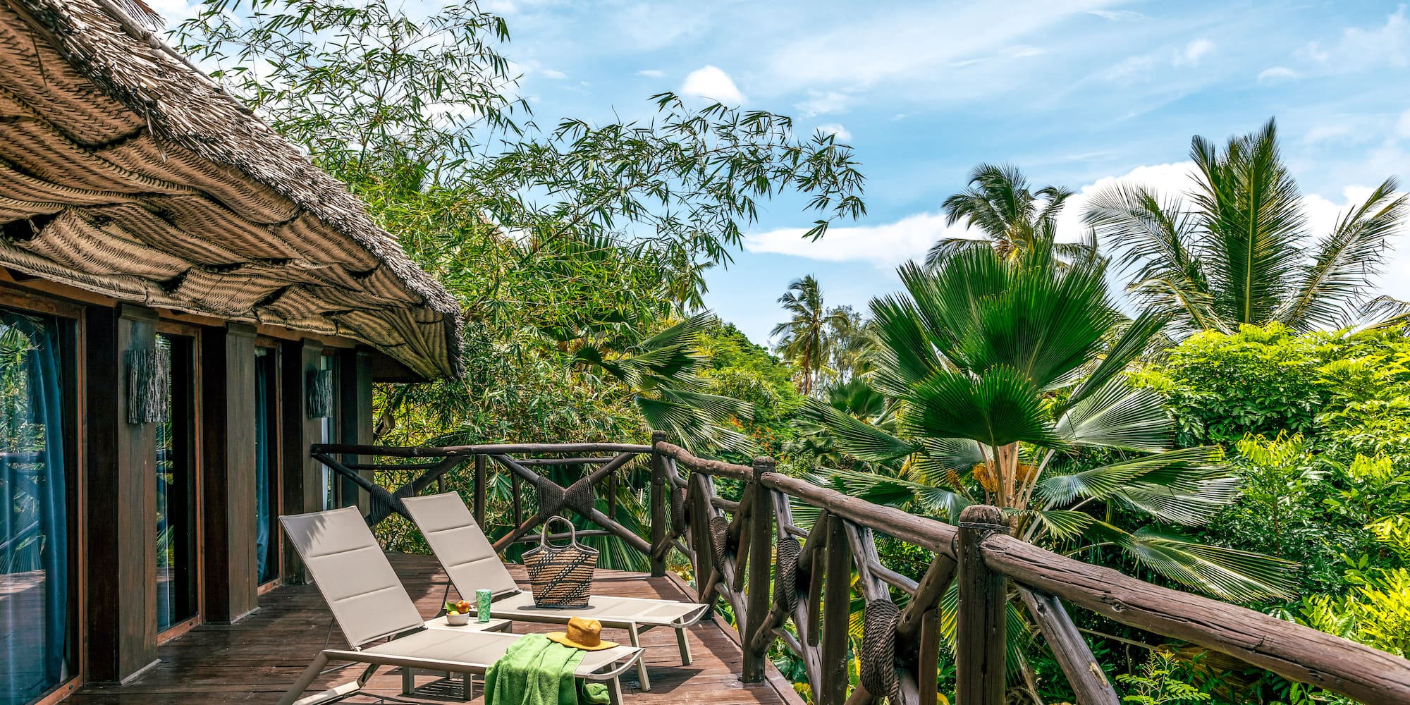 Tropical resort balcony with lounge chairs and lush palm views.