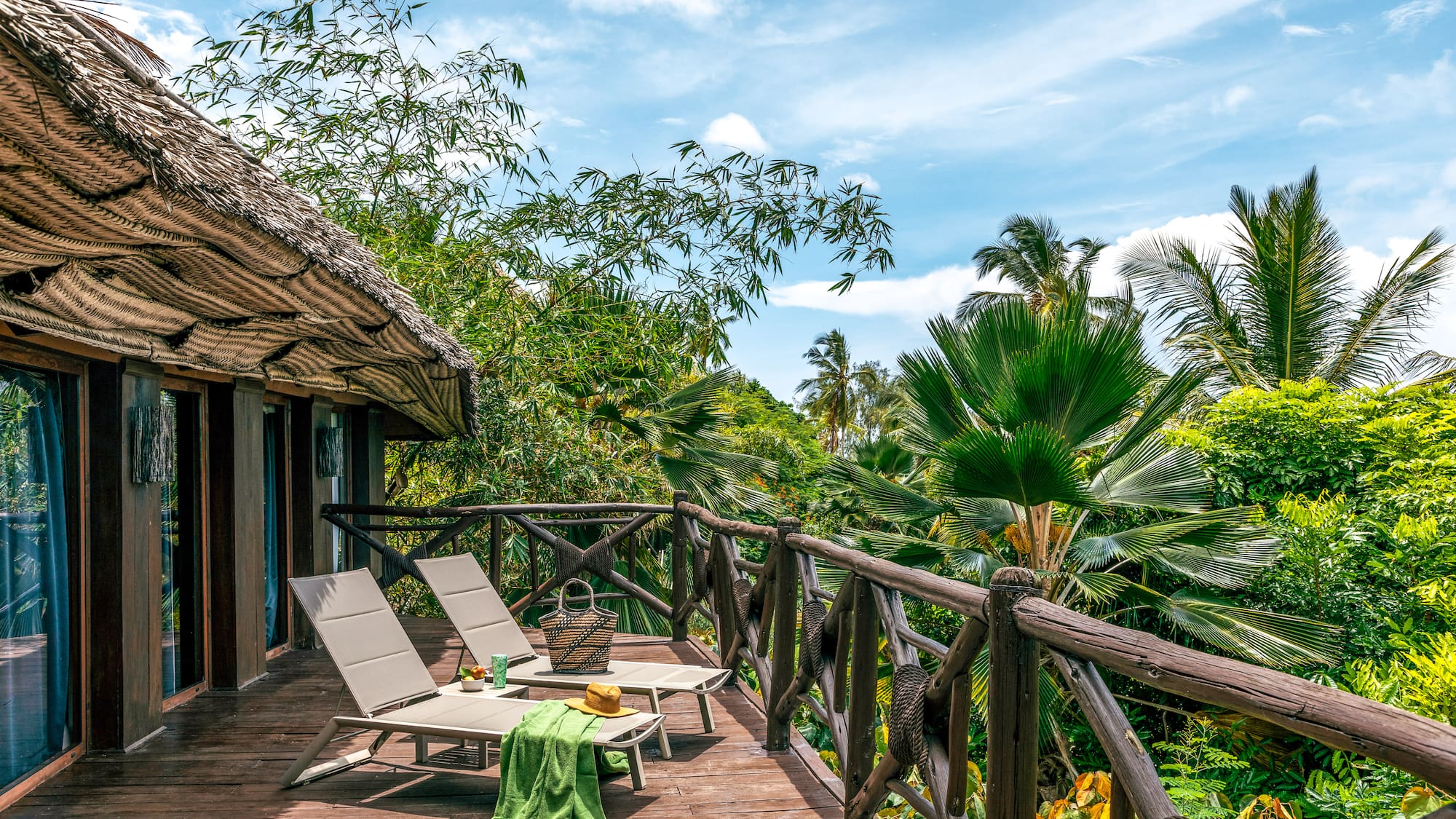 Tropical resort balcony with lounge chairs and lush palm views.