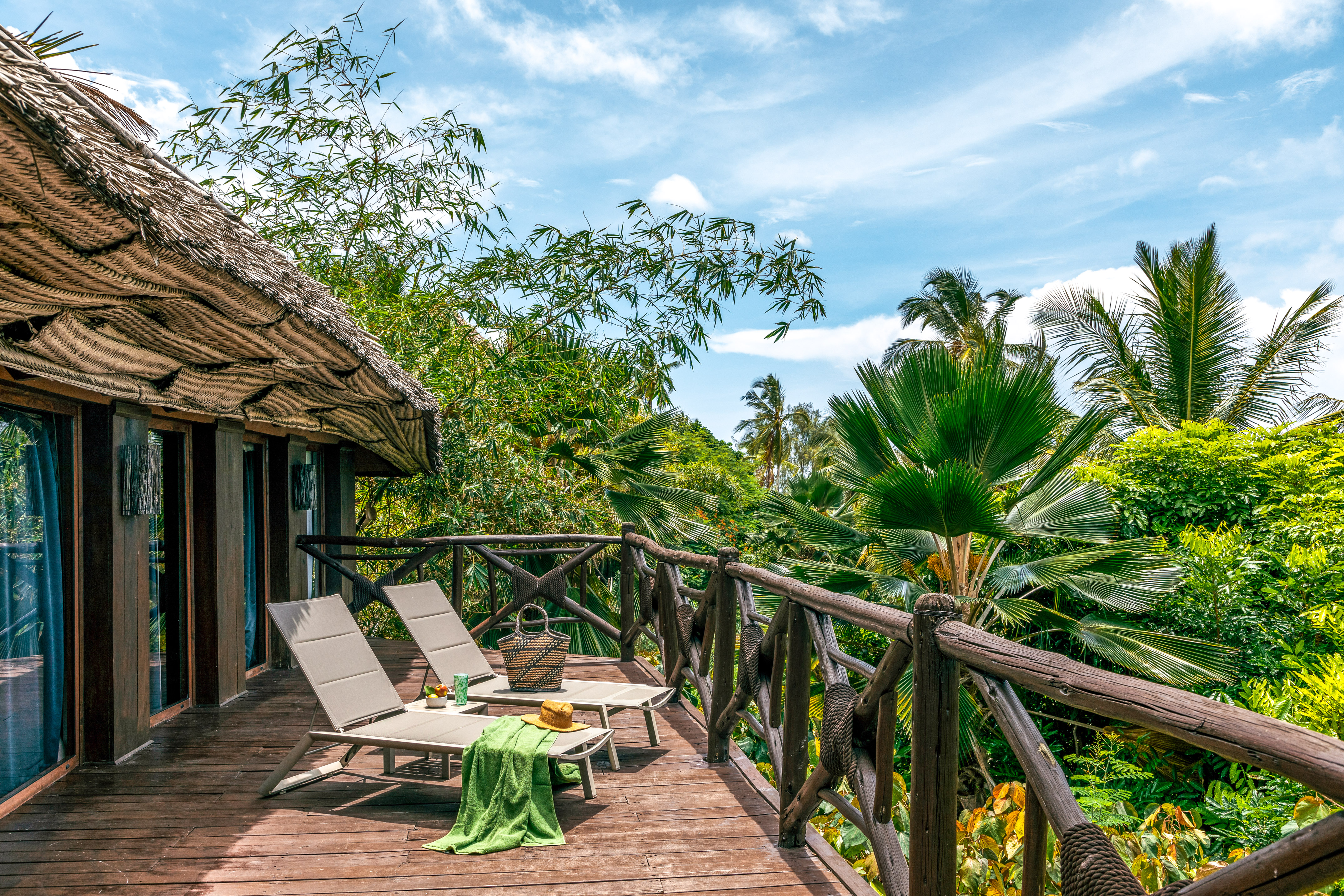 Tropical resort balcony with lounge chairs and lush palm views.