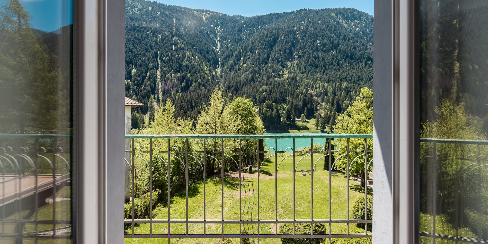 Balcony overlooking mountain lake, green forest, and garden.
