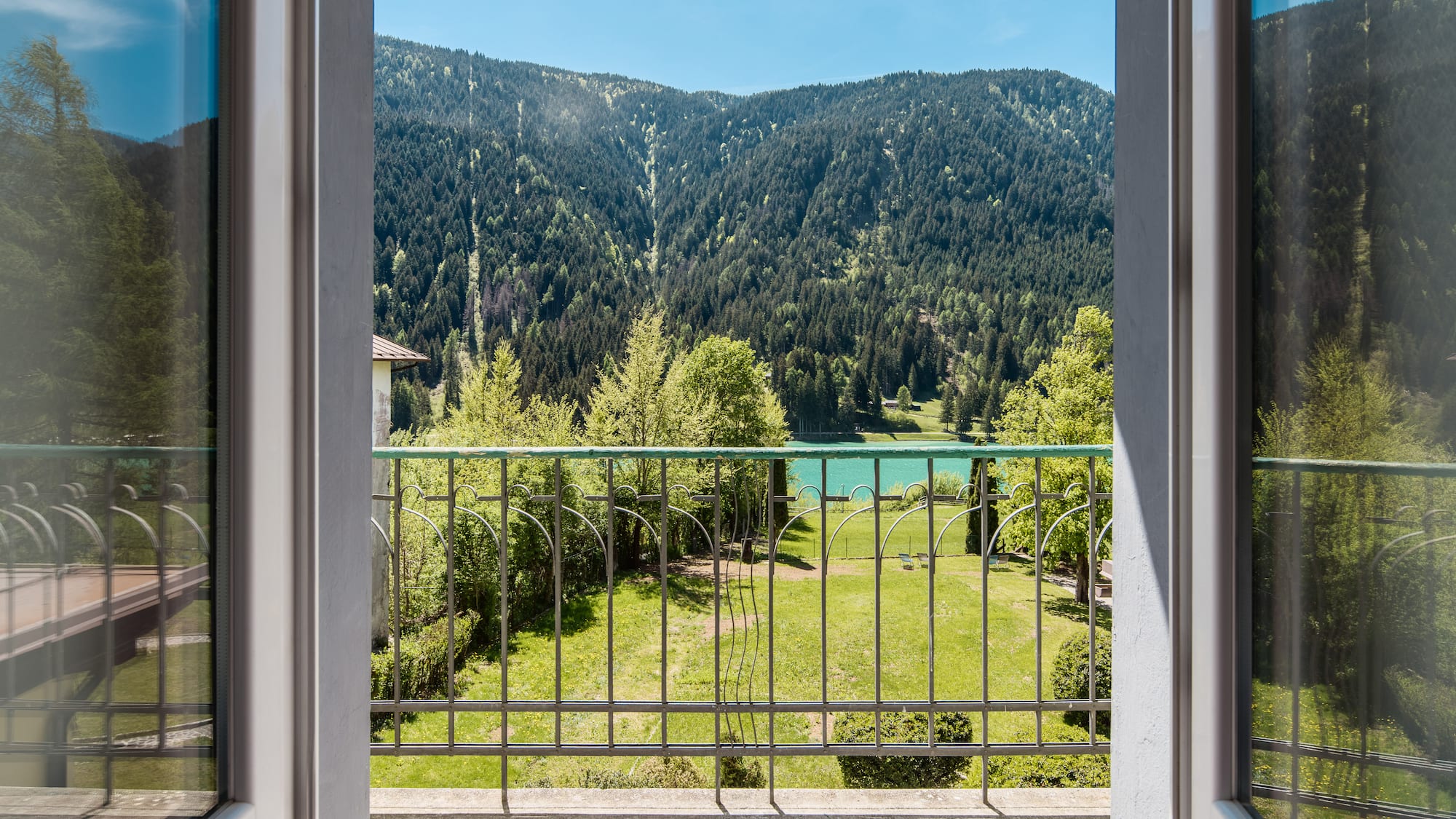 Balcony view of turquoise lake, forested mountains, and green garden.