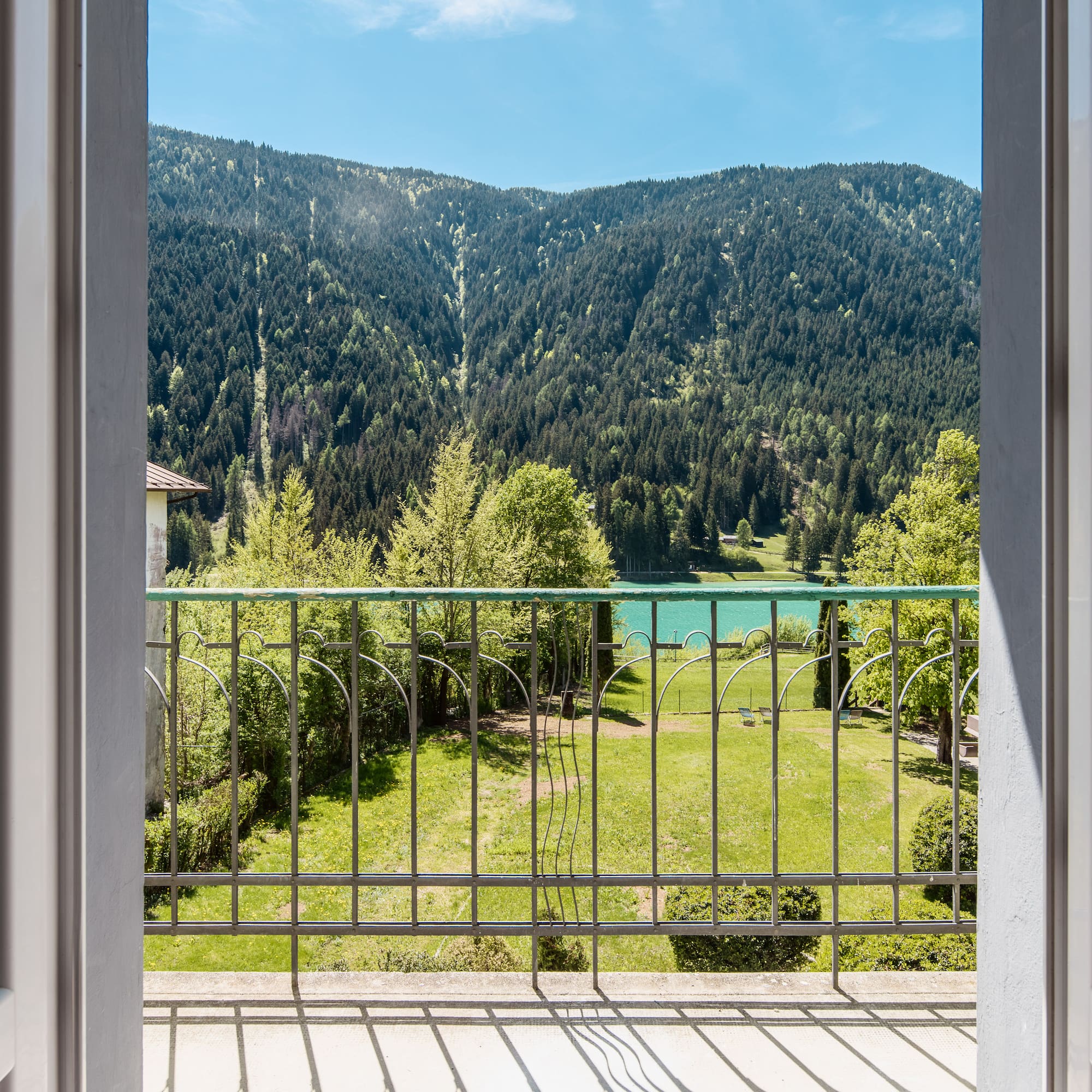 Balcony overlooking mountain lake, green forest, and garden.