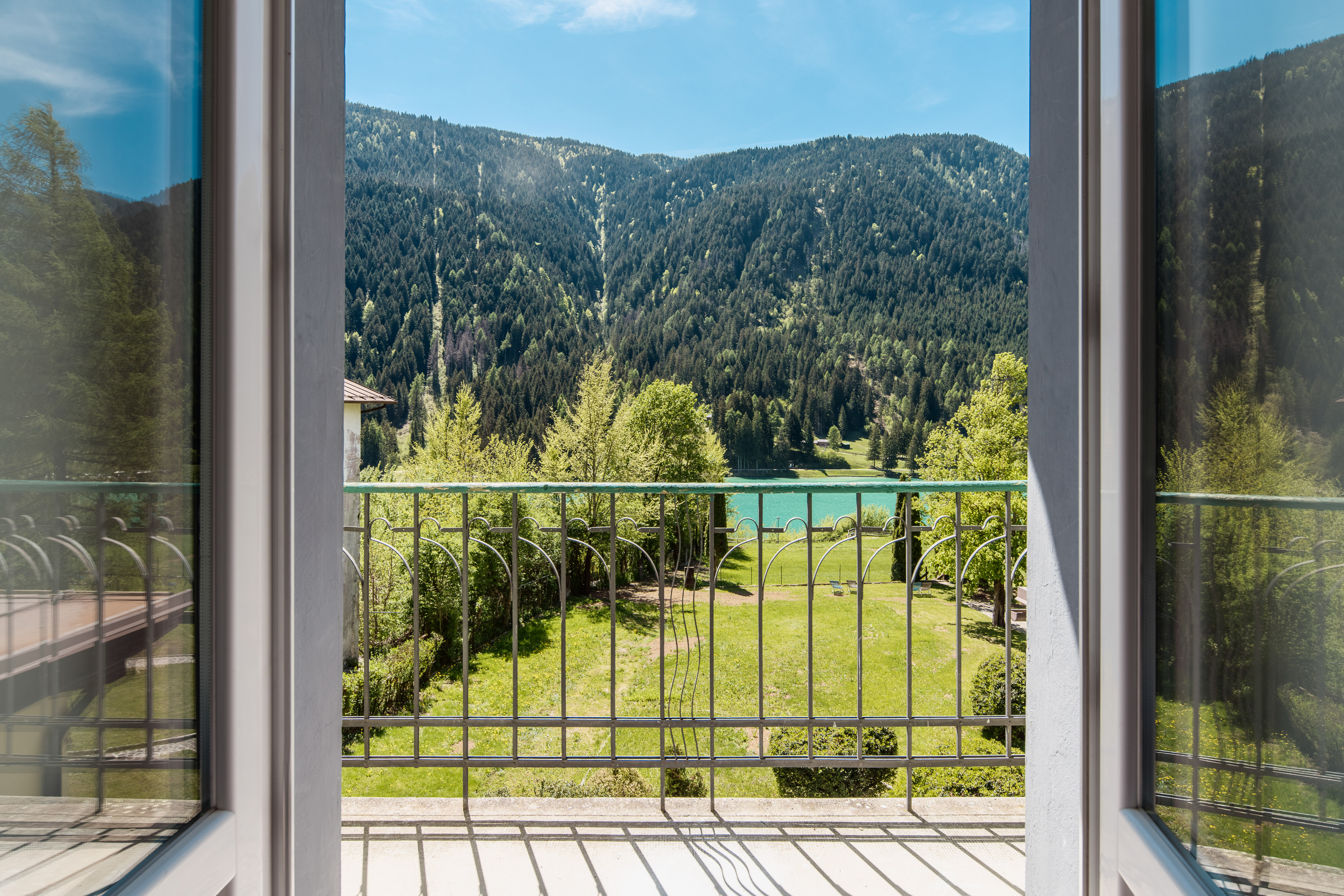 Balcony overlooking mountain lake, green forest, and garden.
