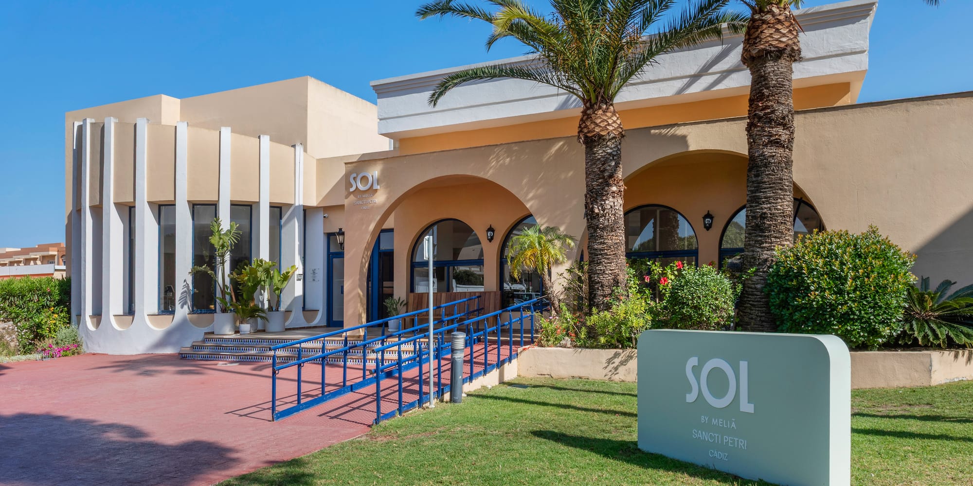 Sol by Meliã Sancti Petri hotel entrance, palm trees, and blue accessibility ramp.