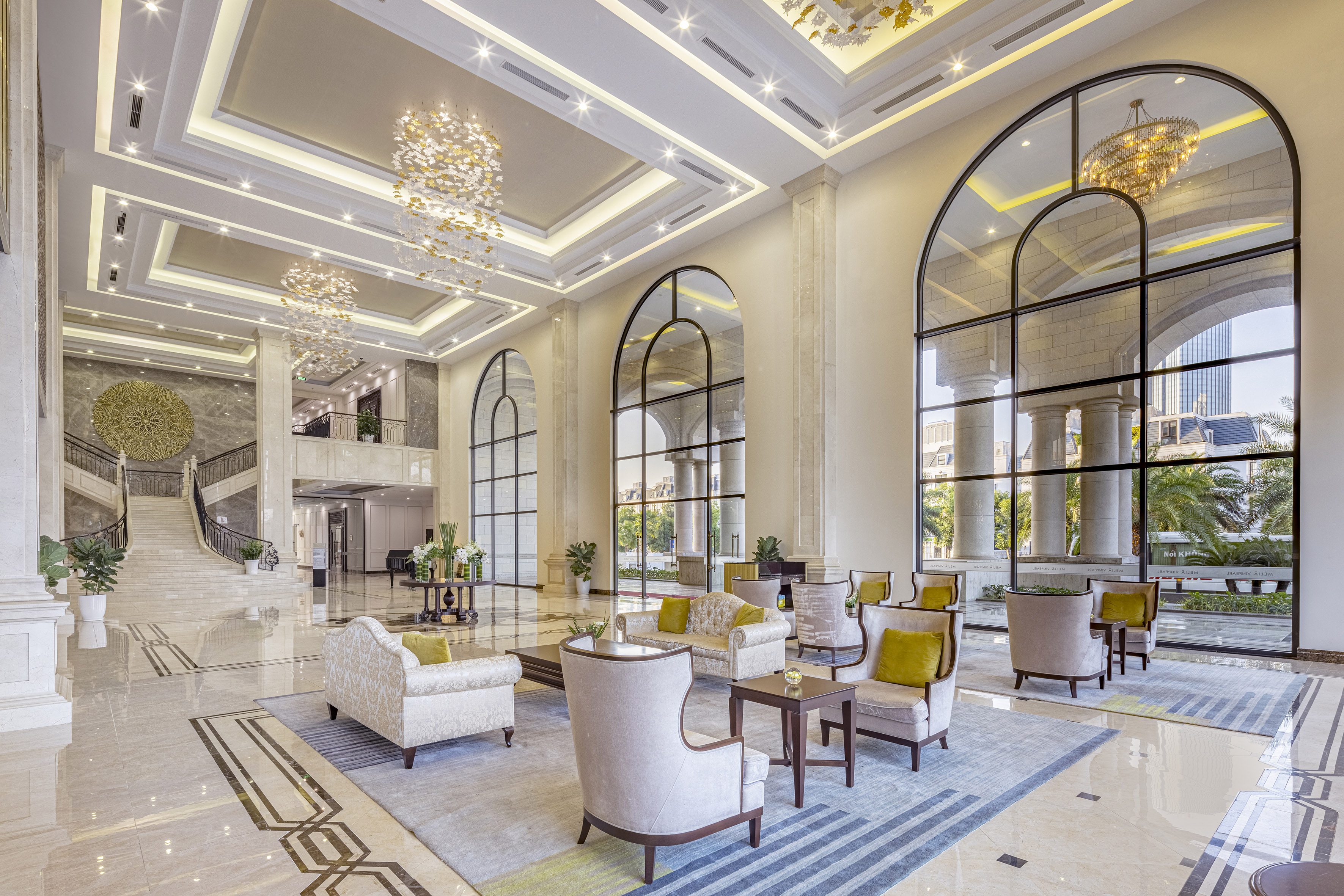 Grand hotel lobby, ornate chandeliers, elegant seating, and arched windows.