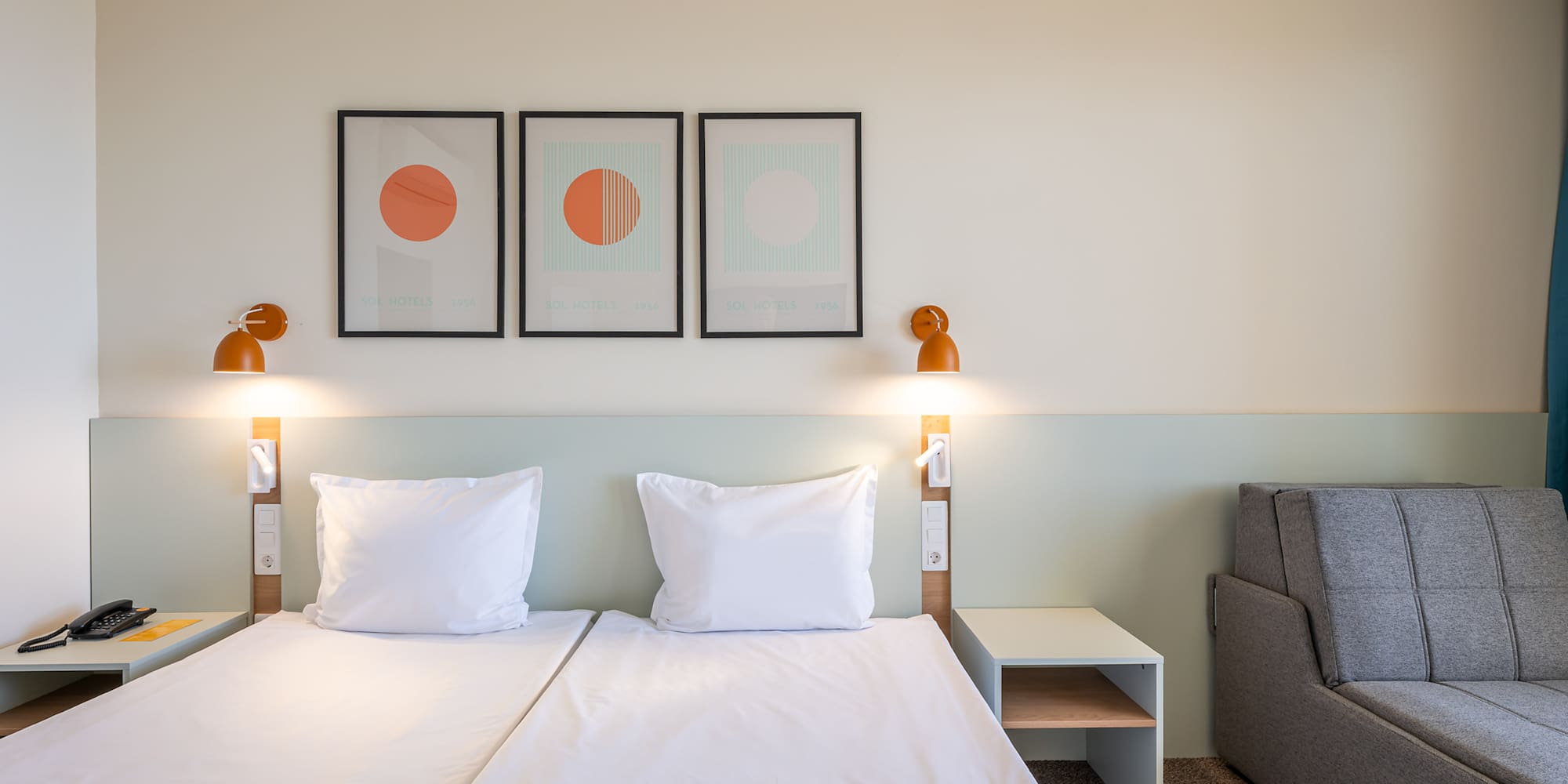 Modern hotel room with twin beds, abstract wall art, and sofa.