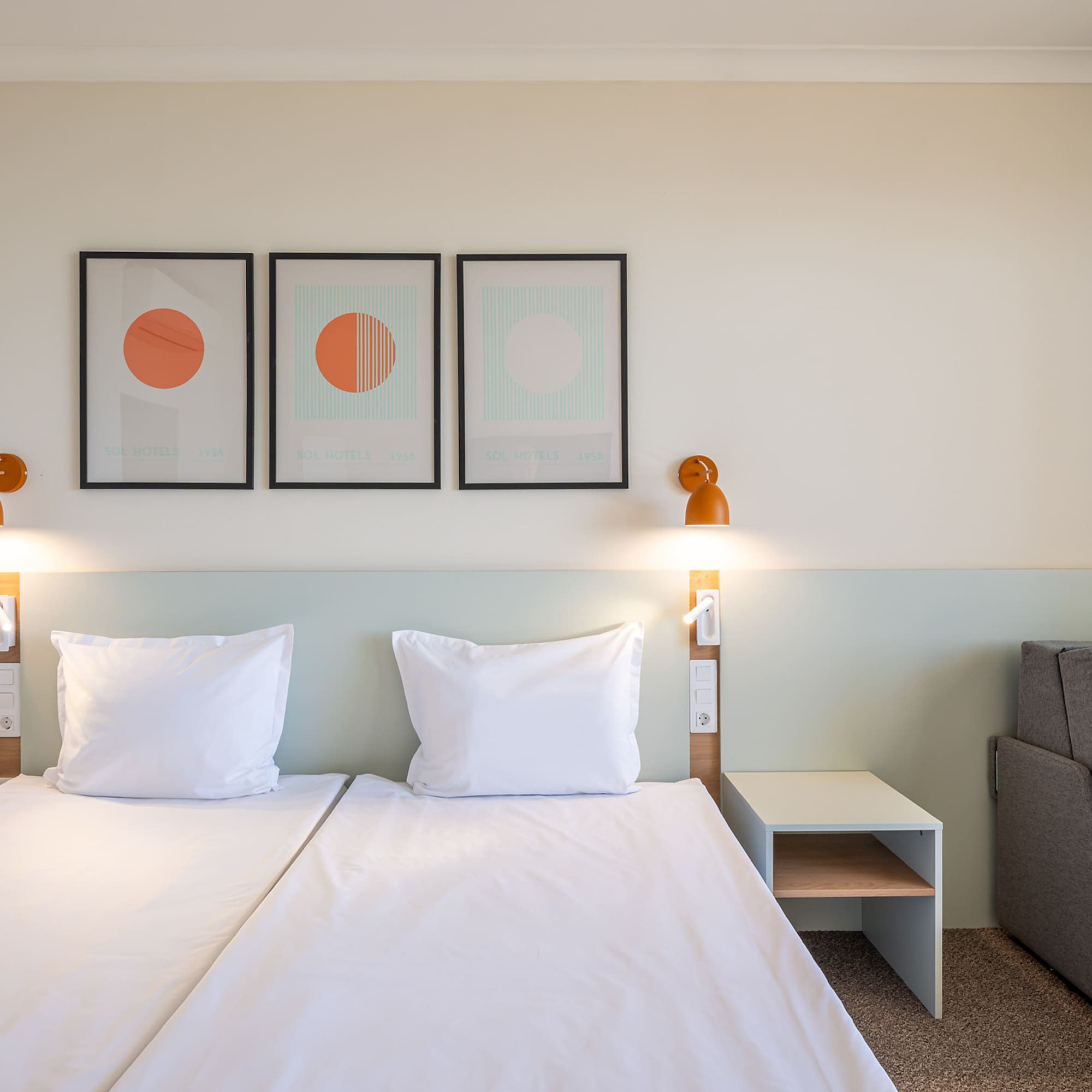 Modern hotel room with twin beds, abstract wall art, and sofa.