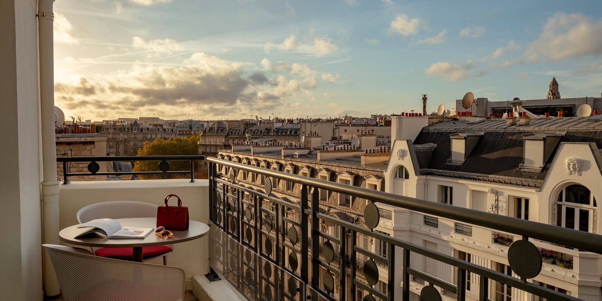 a balcony with a table and chairs and a railing with a city in the background