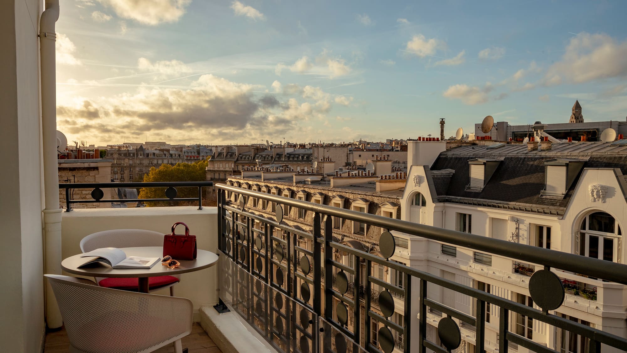 a balcony with a table and chairs and a railing with a city in the background