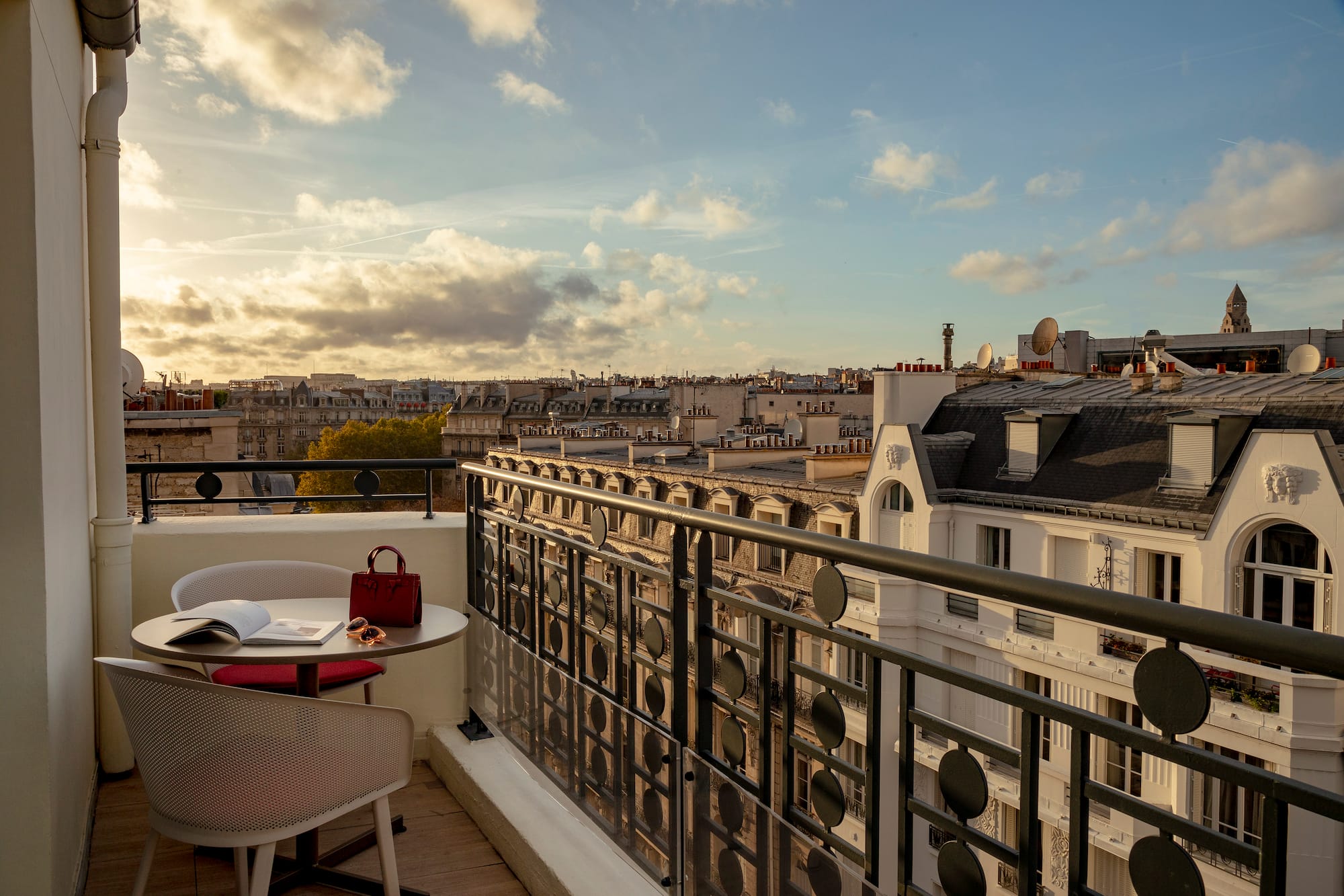 a balcony with a table and chairs and a railing with a city in the background