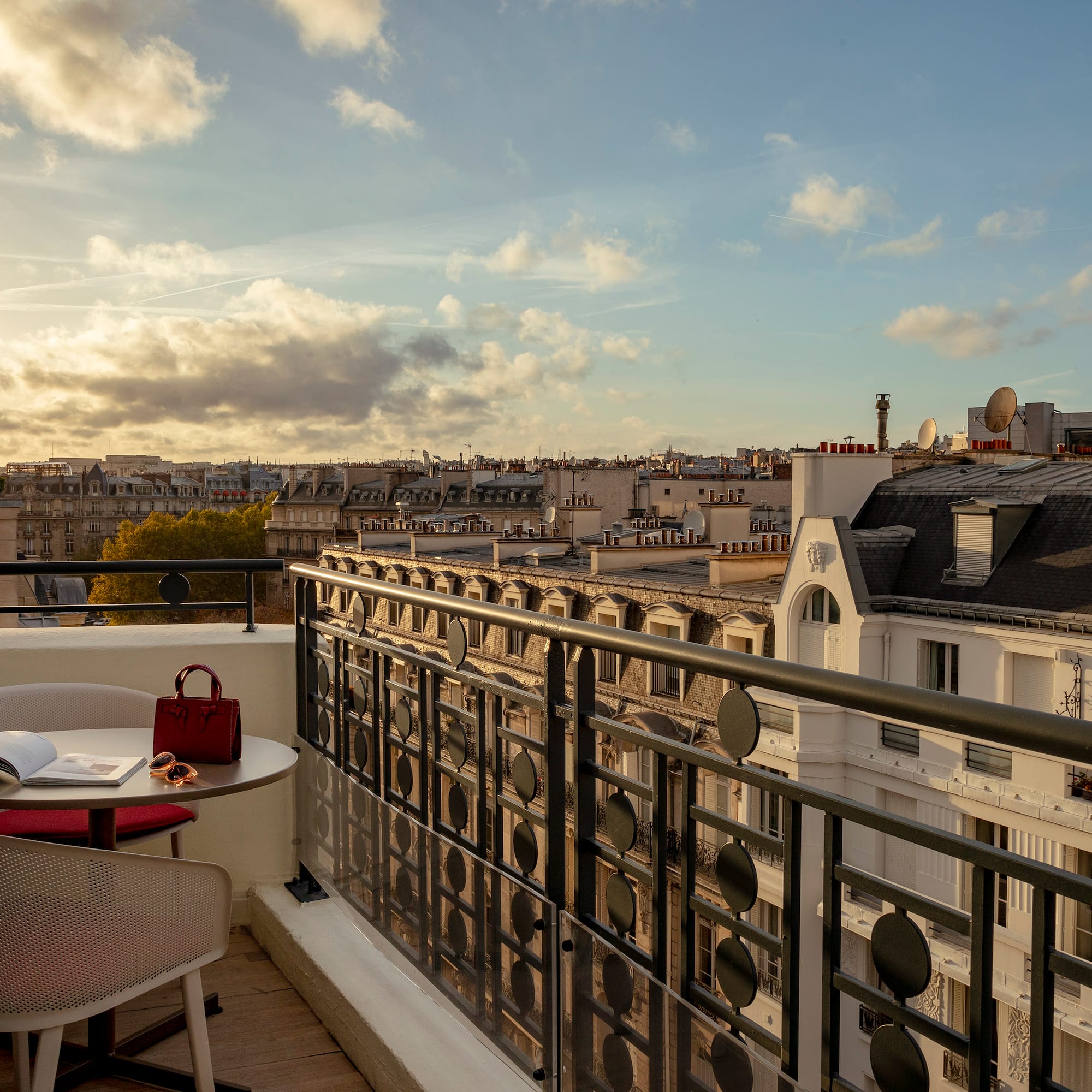 a balcony with a table and chairs and a railing with a city in the background