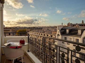 a balcony with a table and chairs and a railing with a city in the background