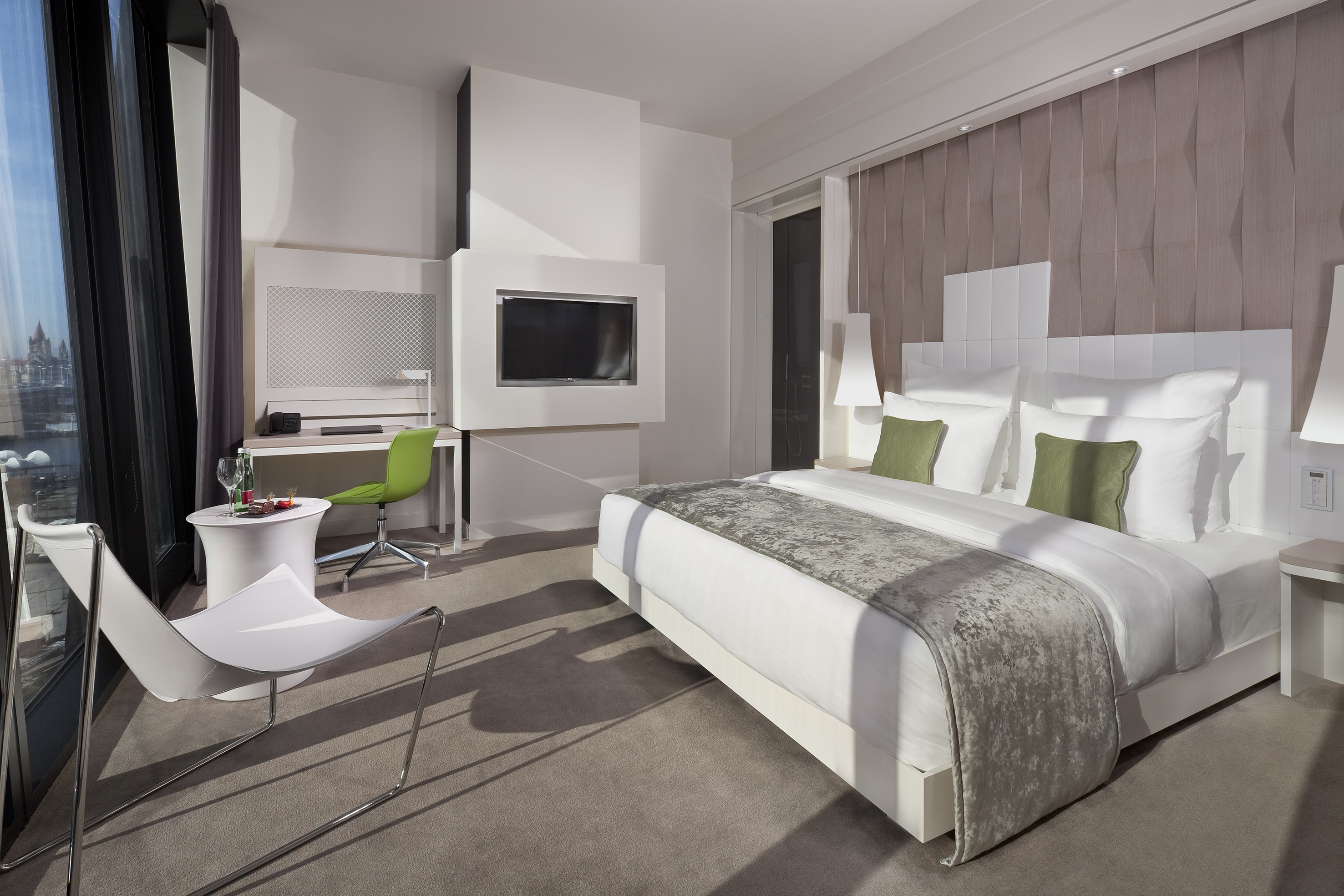 Contemporary hotel suite with large bed, desk, wall TV, and city view.