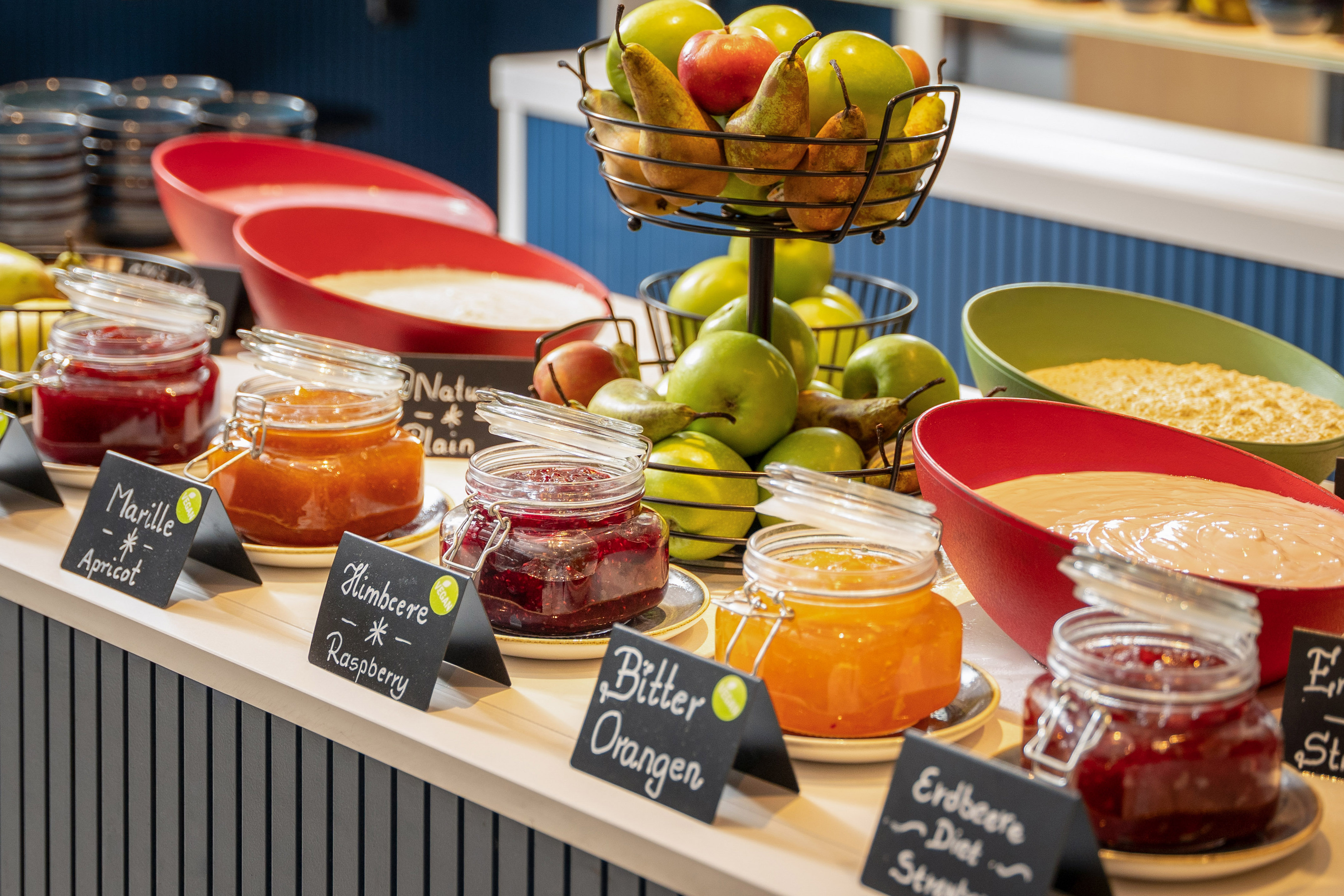Breakfast buffet with various fruit jams, fresh apples, pears, and yogurt bowls.