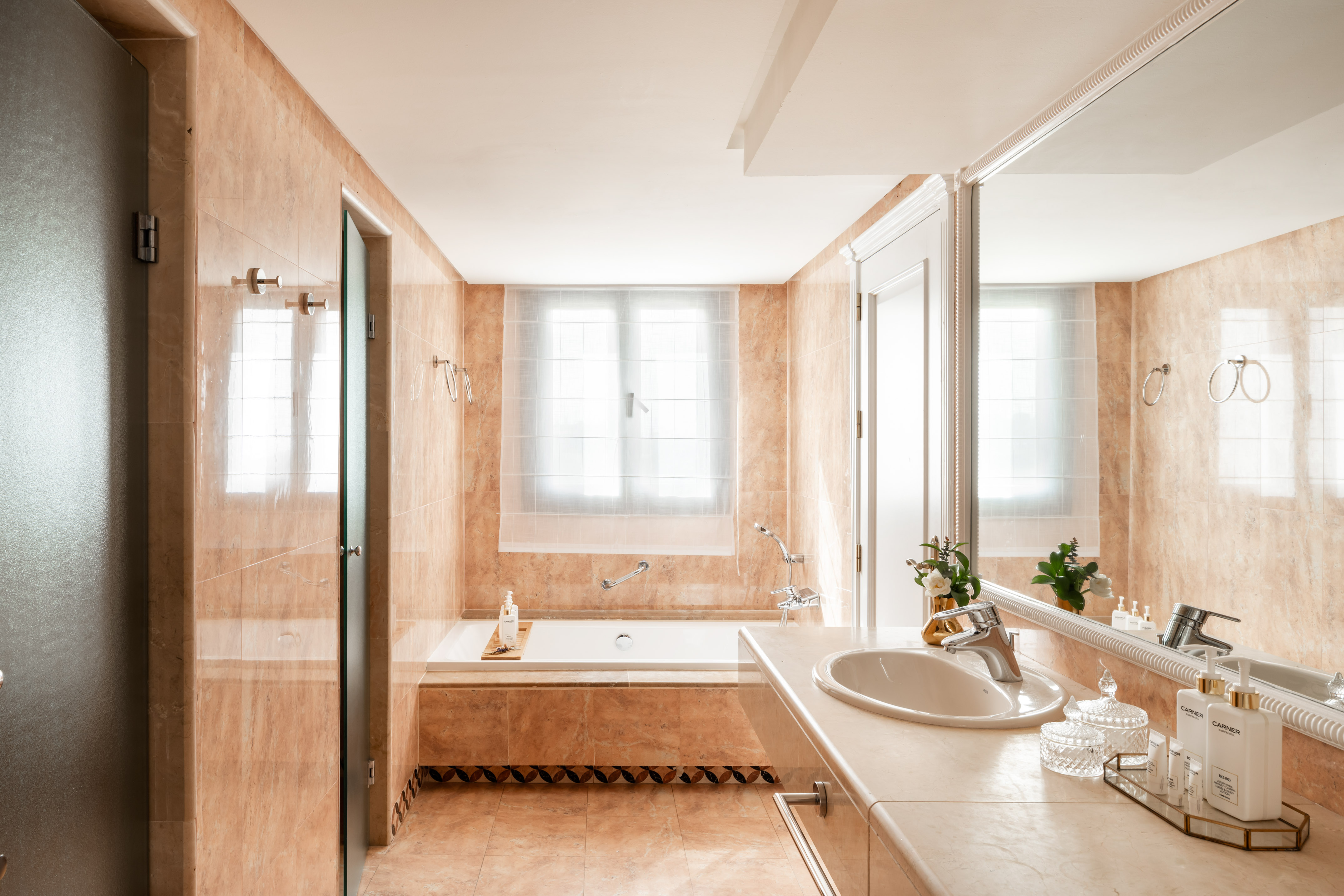 Modern peach marble bathroom with deep bathtub, vanity, and large mirror.
