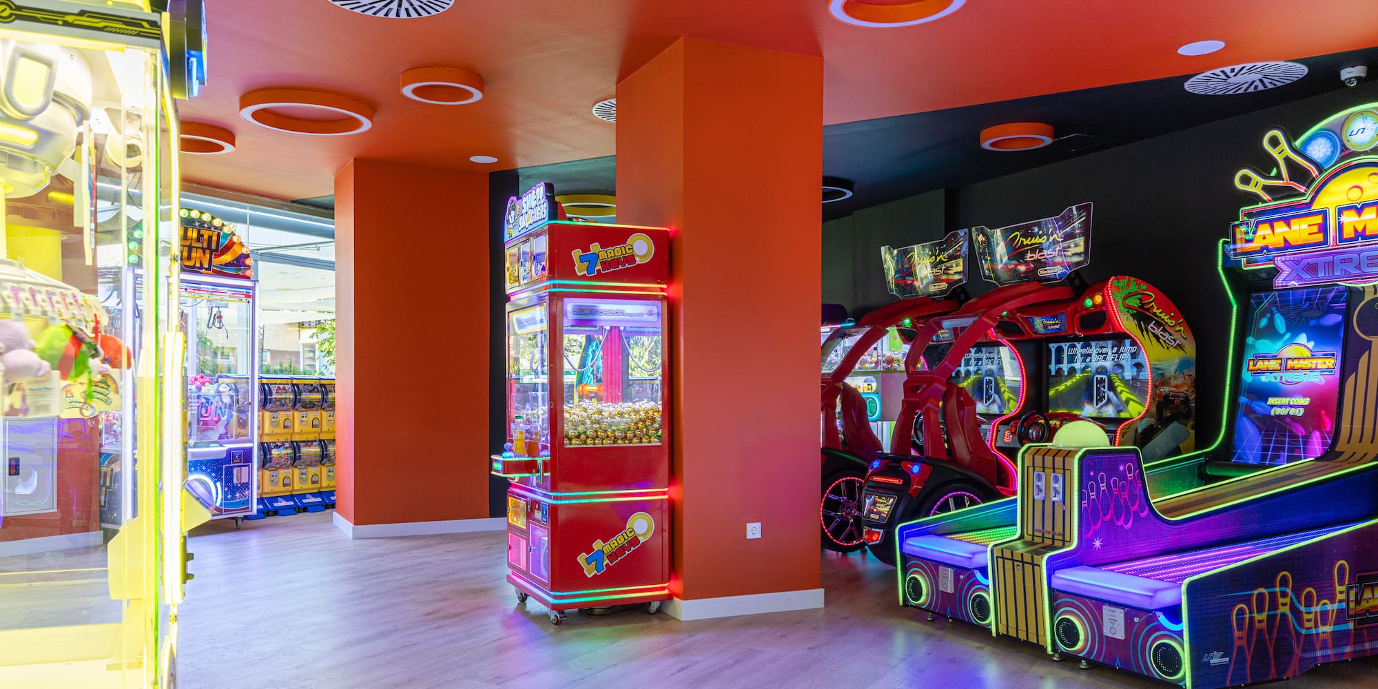 Modern arcade game room with neon-lit claw machines, racing, and bowling games.