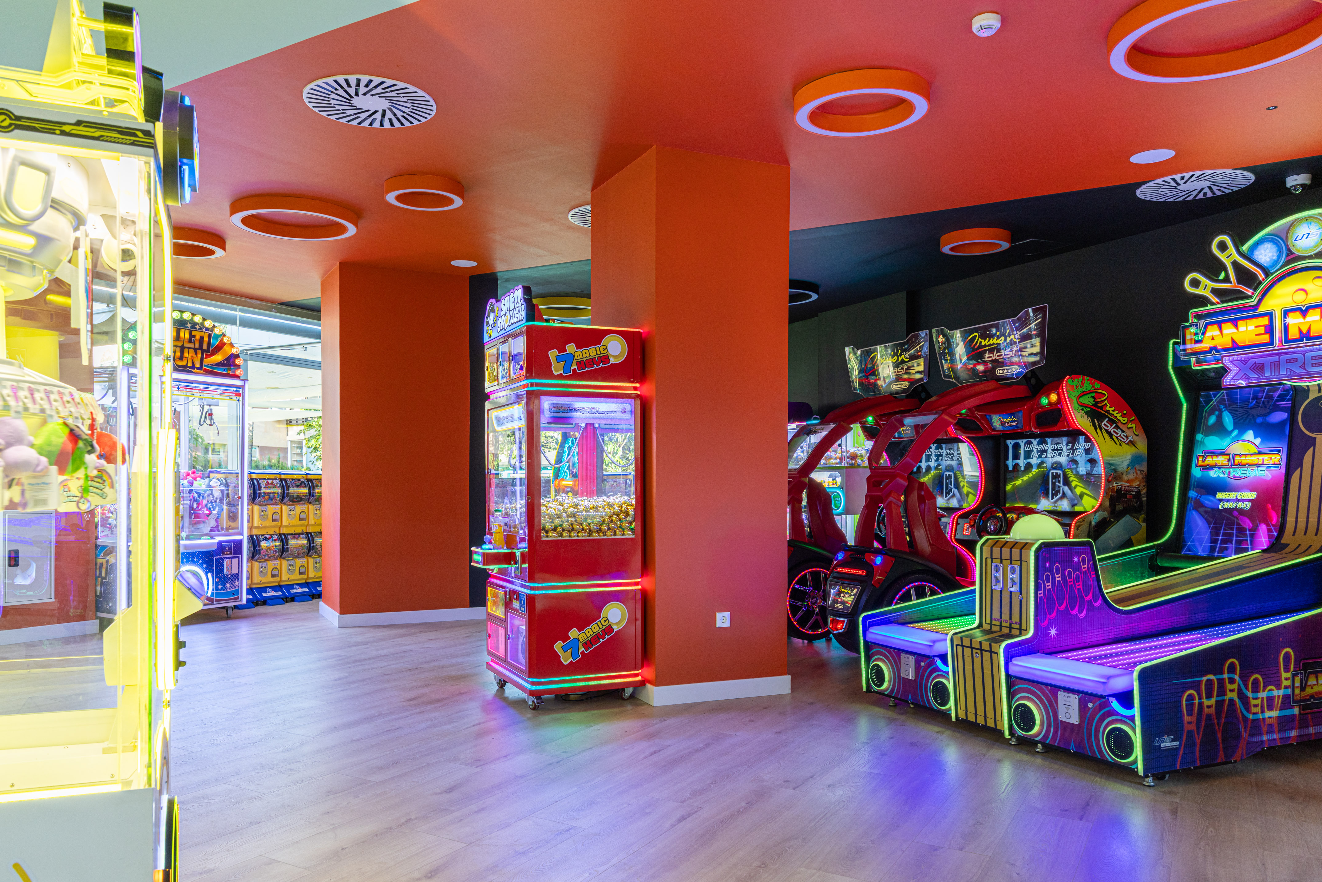 Modern arcade game room with neon-lit claw machines, racing, and bowling games.