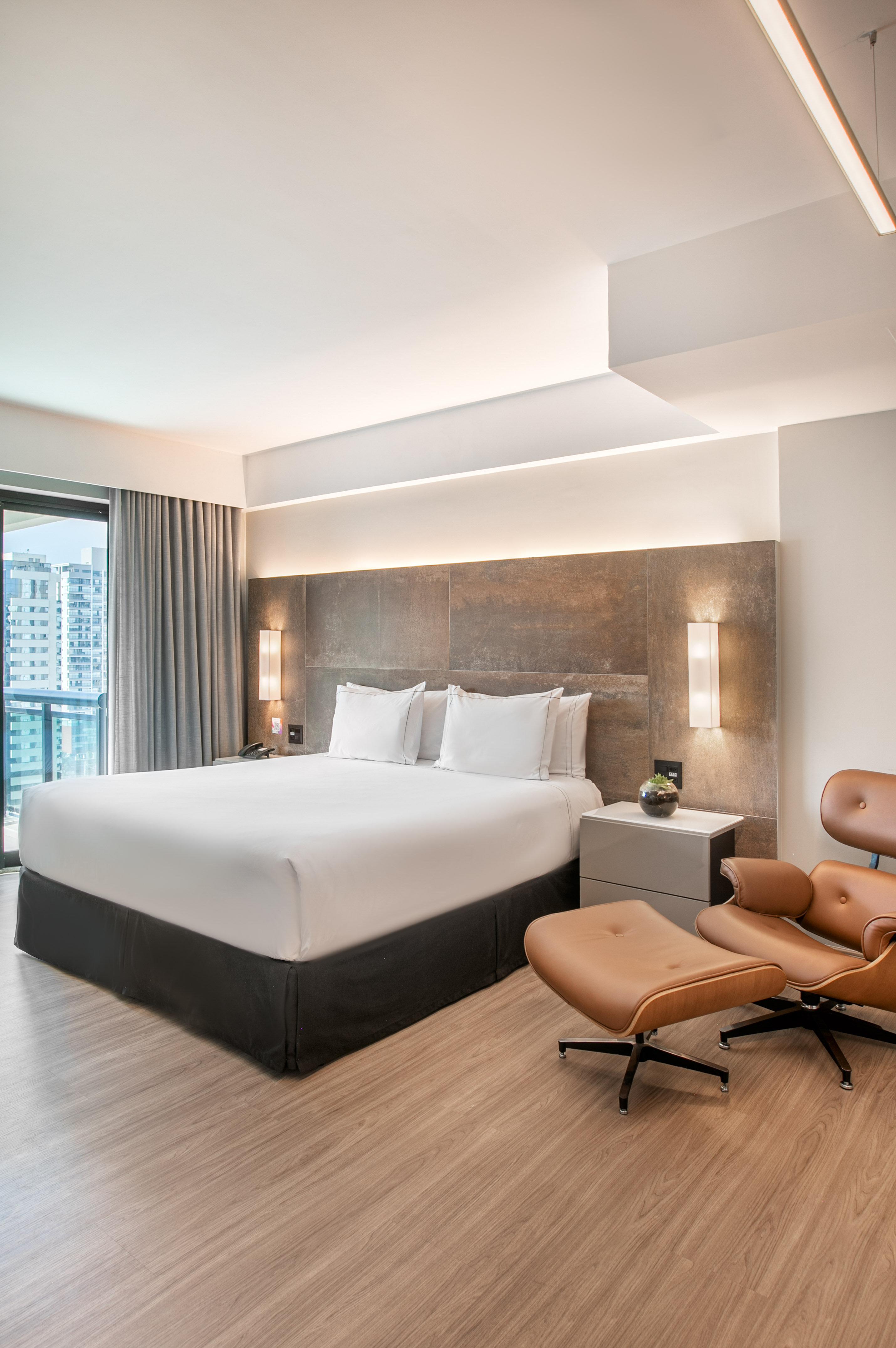 Luxury hotel bedroom with king bed, city view, and leather lounge chair.