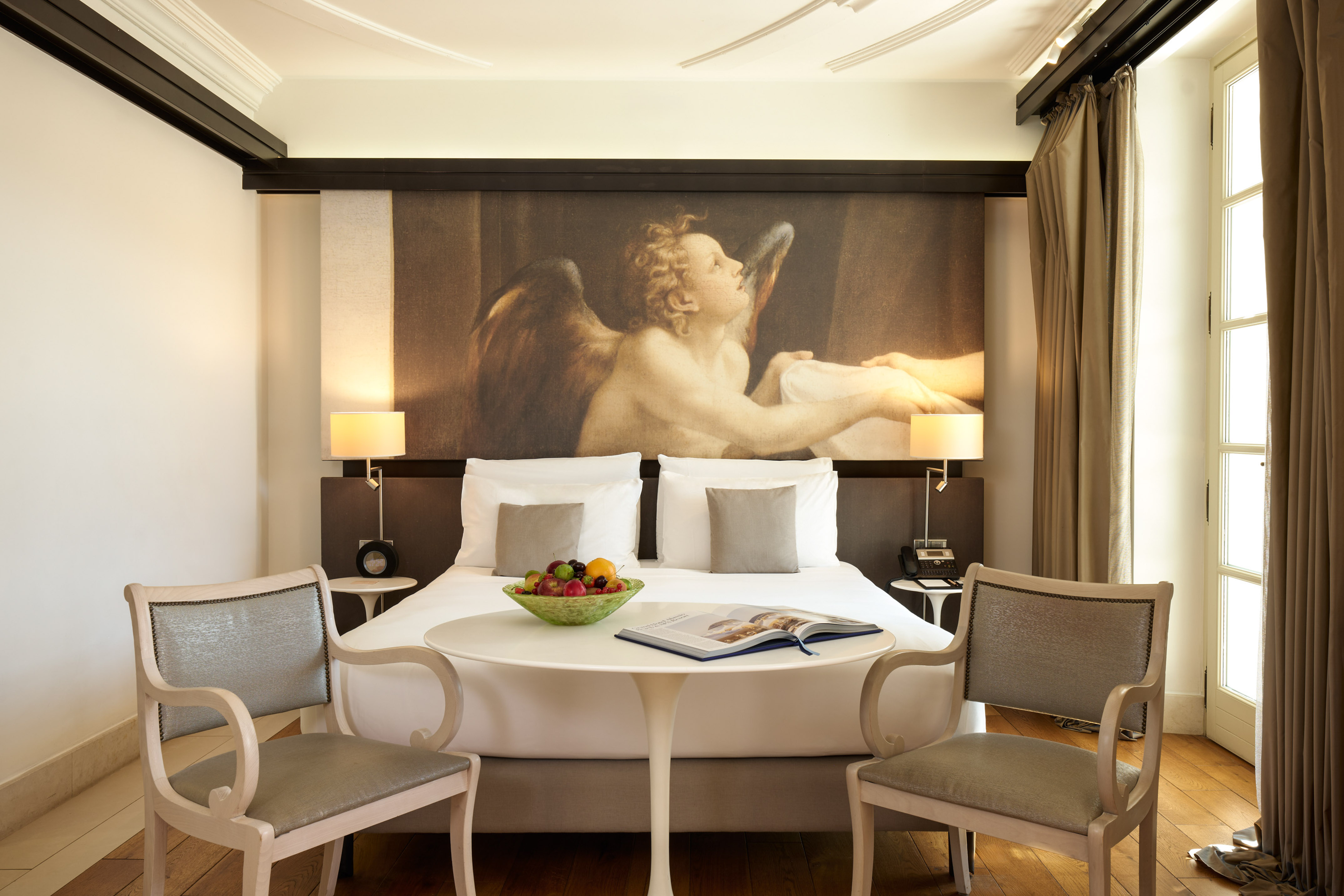 Elegant hotel room featuring a large bed, angel mural, and seating area.
