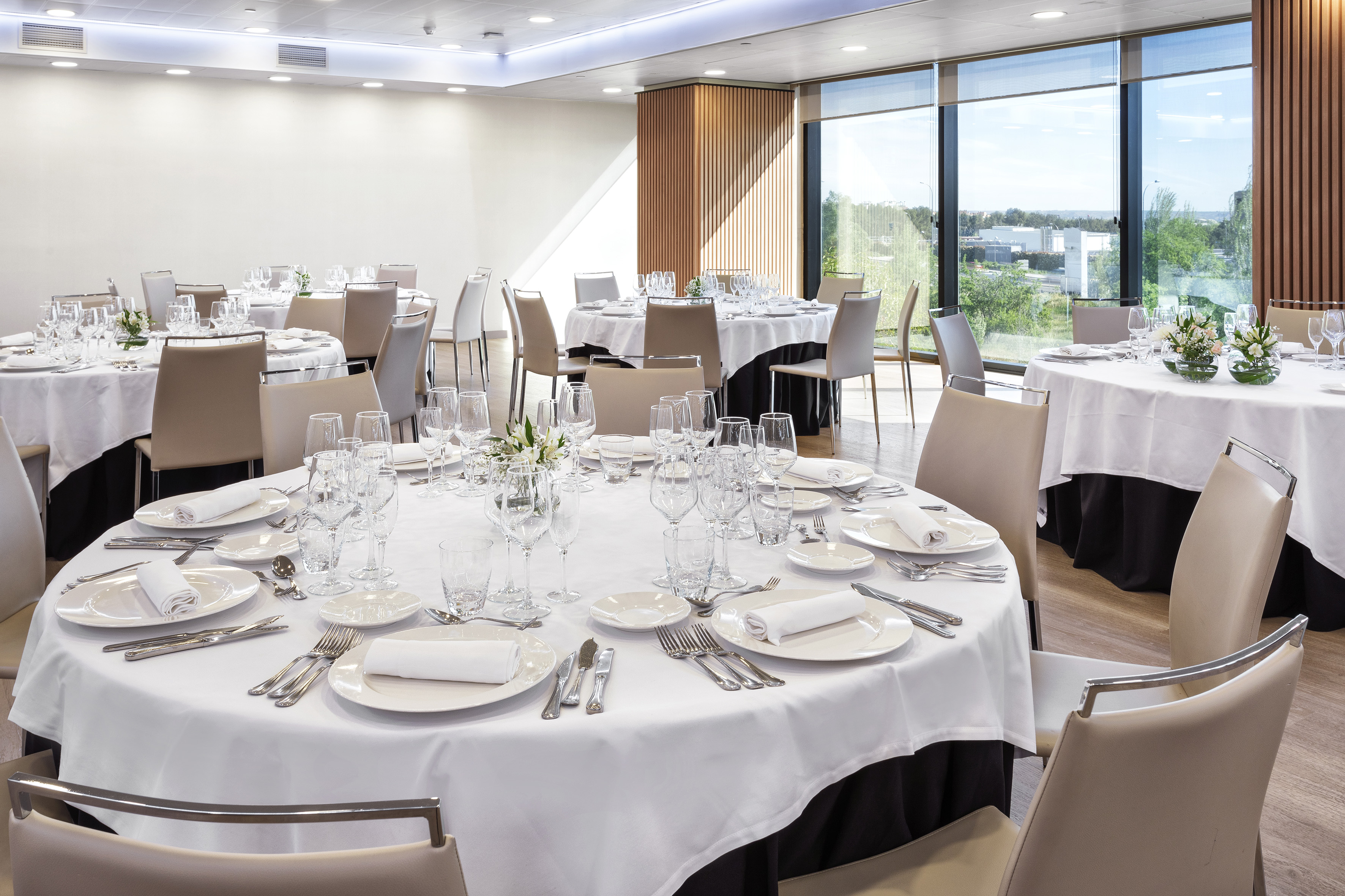 Modern banquet hall with elegantly set round tables and large windows.