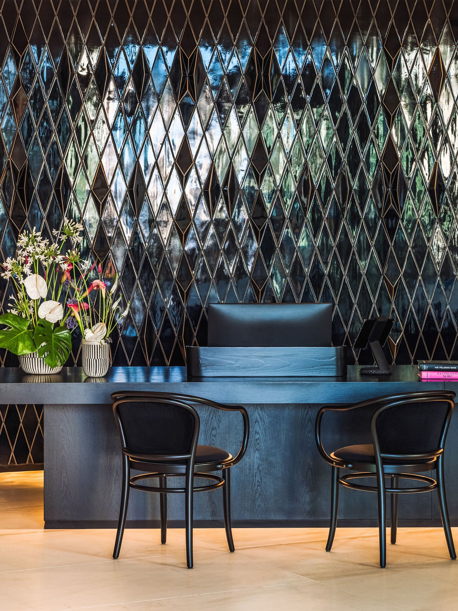 Modern black reception desk with reflective diamond wall tiles and chairs.