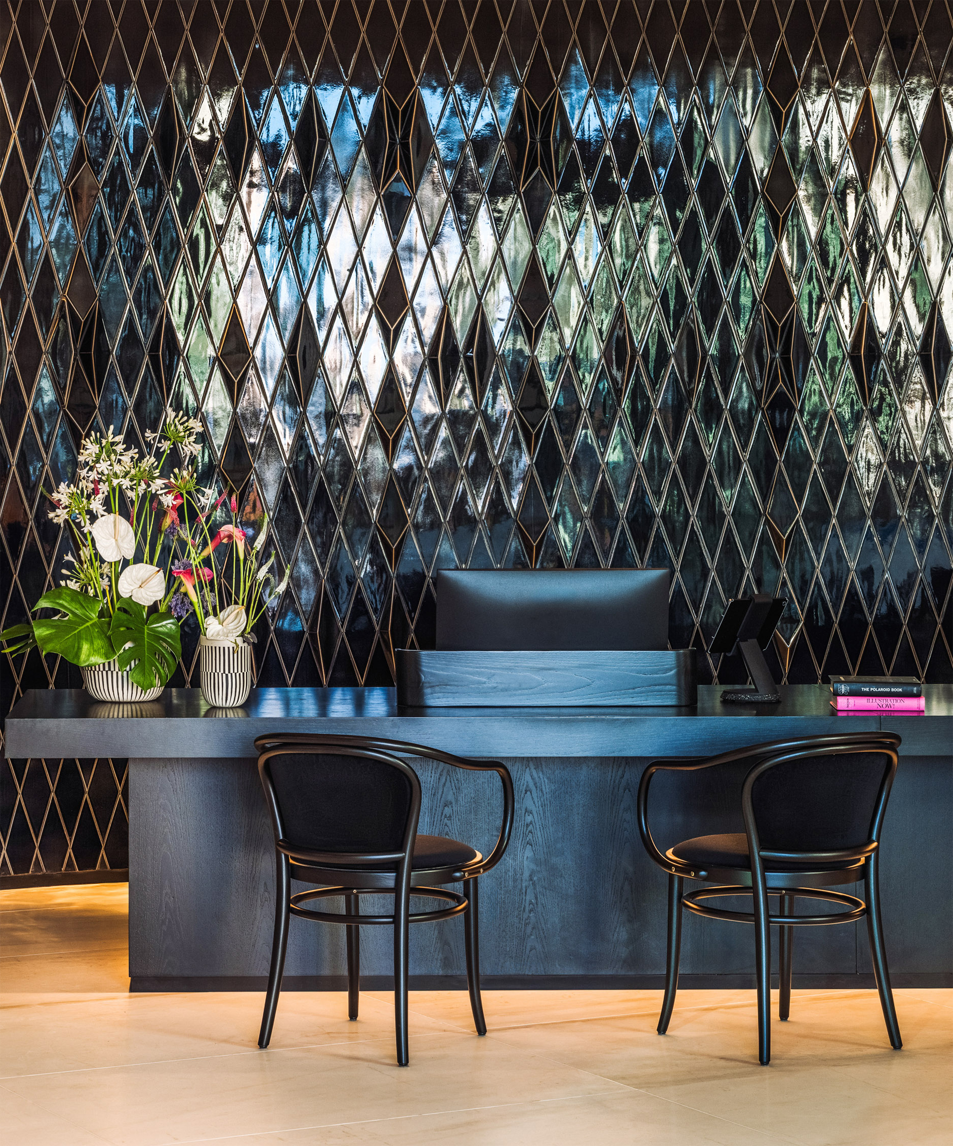 Modern black reception desk with reflective diamond wall tiles and chairs.