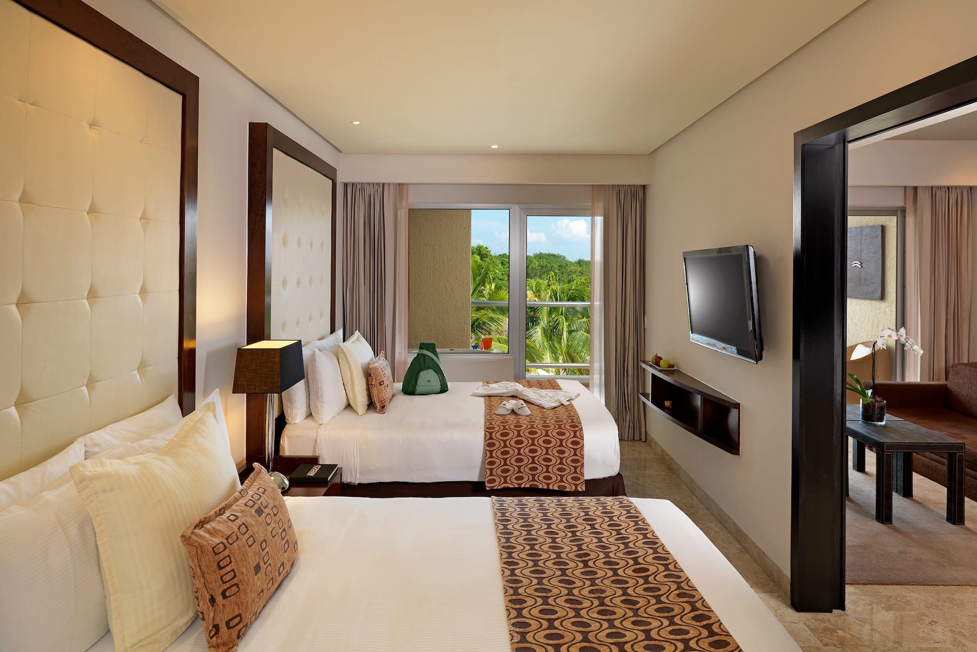 Hotel room with two queen beds, tropical view, TV, and separate living area.