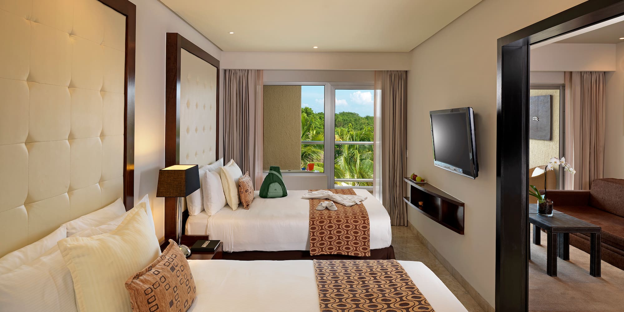 Hotel room with two queen beds, tropical view, TV, and separate living area.