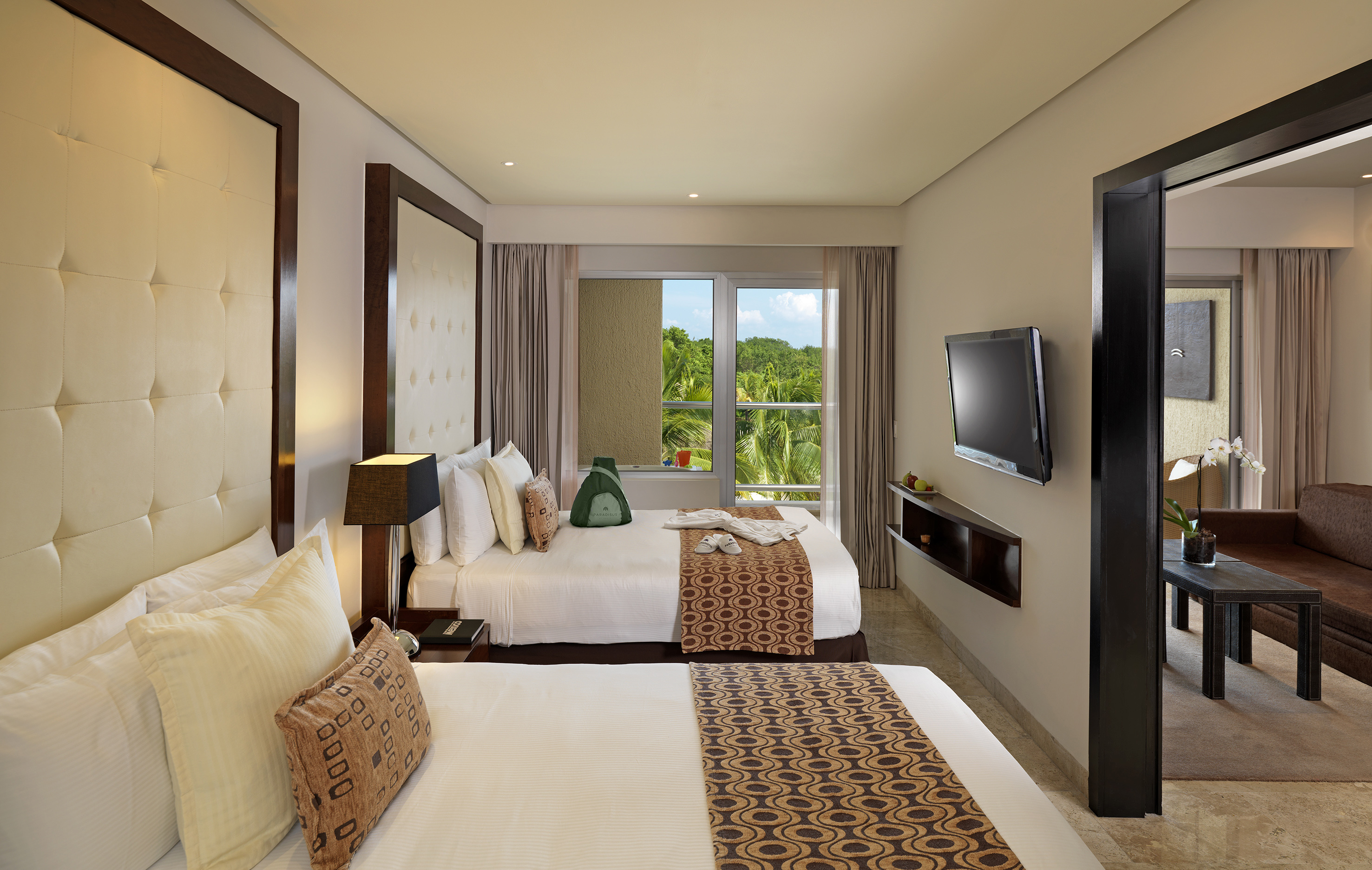 Hotel room with two queen beds, tropical view, TV, and separate living area.