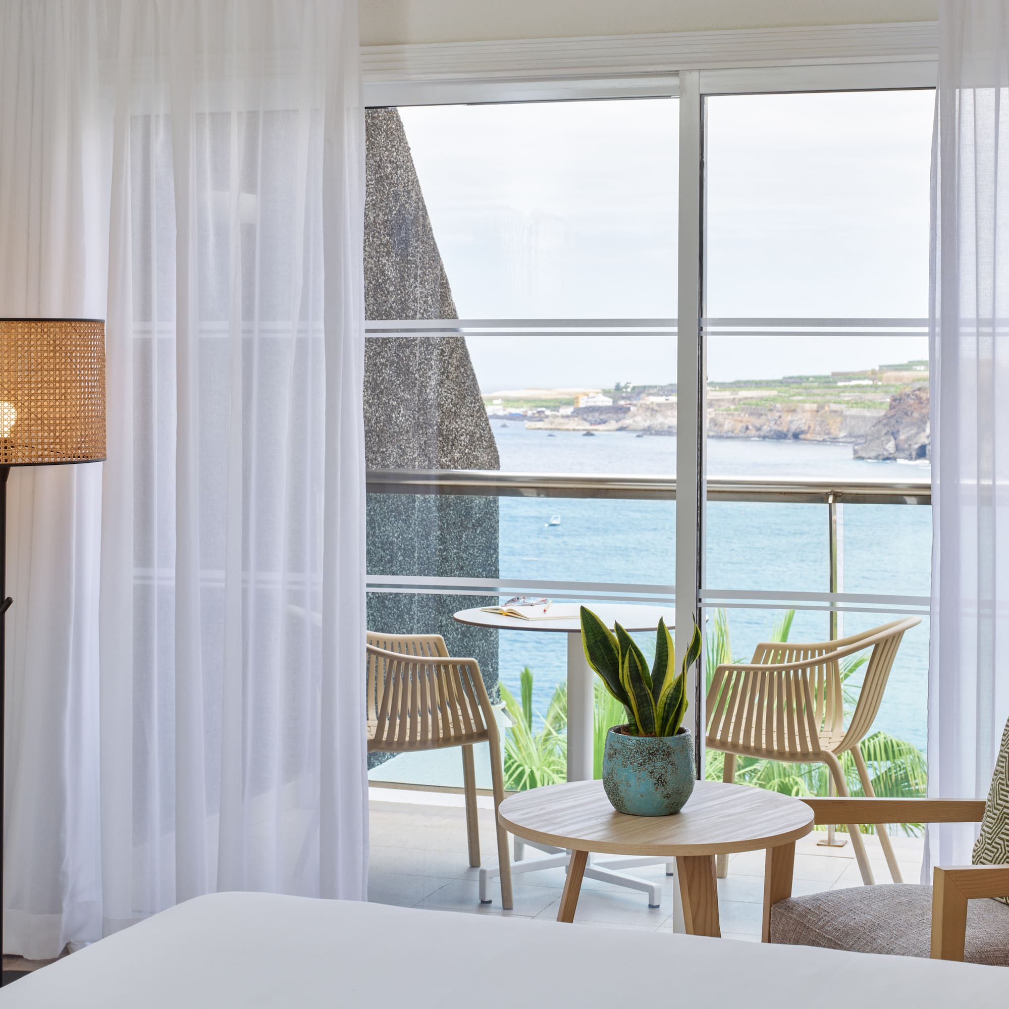 a room with a bed and chairs and a table with a view of the ocean